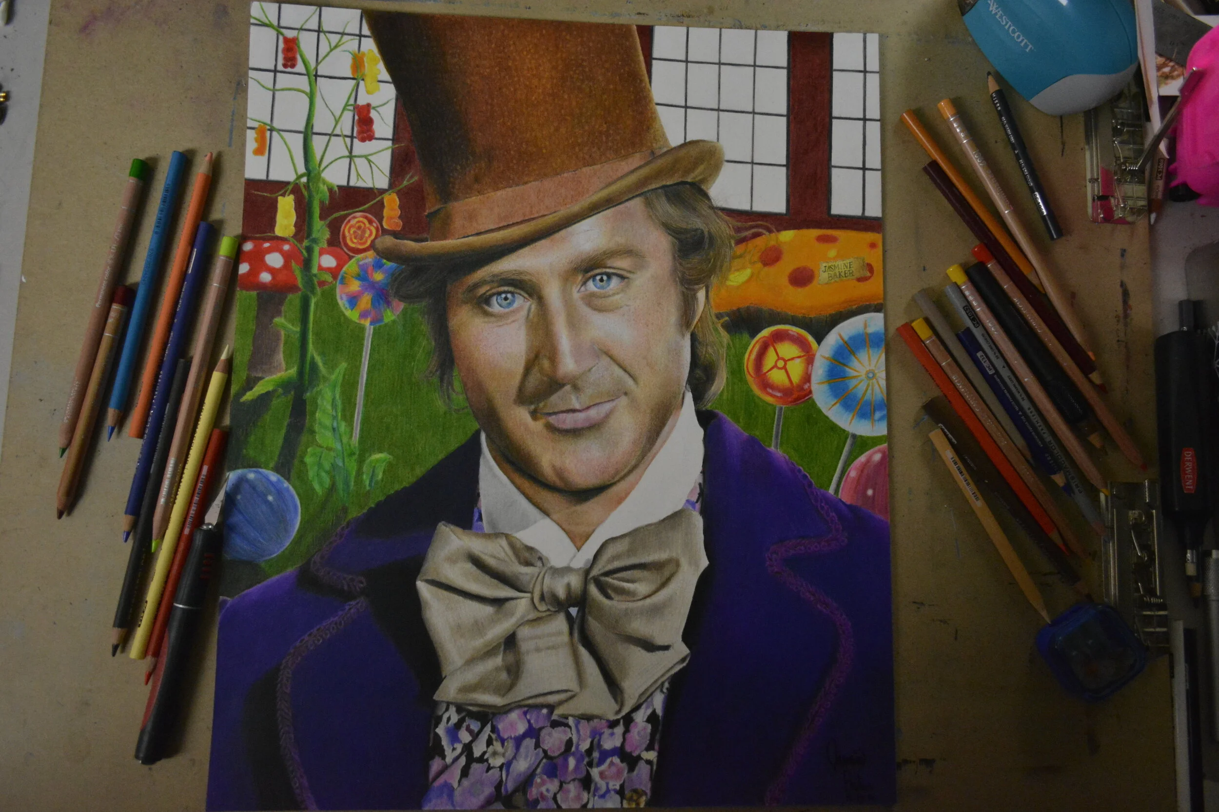 Artwork depicting a man in a brown top hat and purple coat, surrounded by colorful candy-themed scenery, with colored pencils and art supplies on the sides.