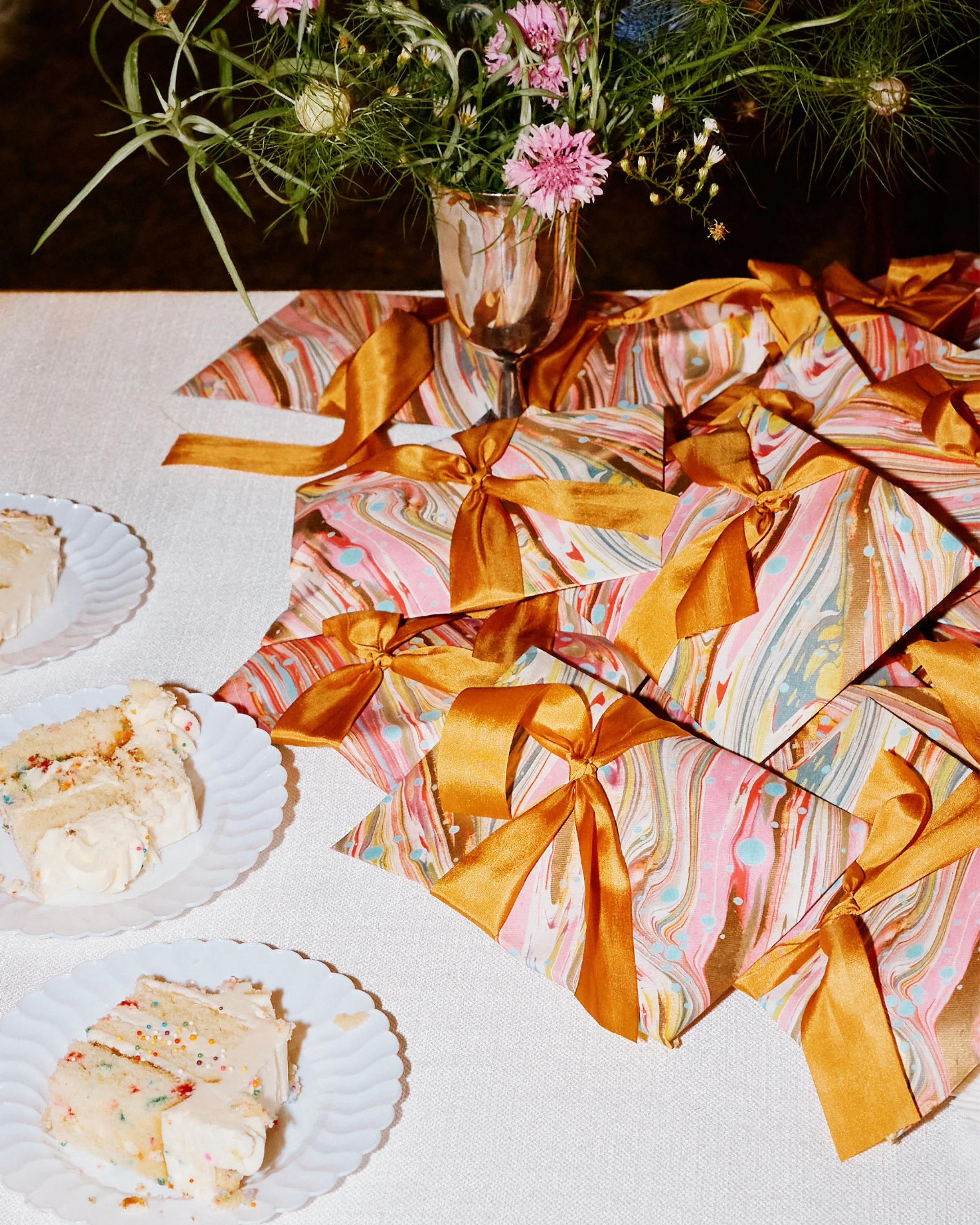 Marbled gift envelopes on a table with slices of cake and small floral arrangement with nettle
