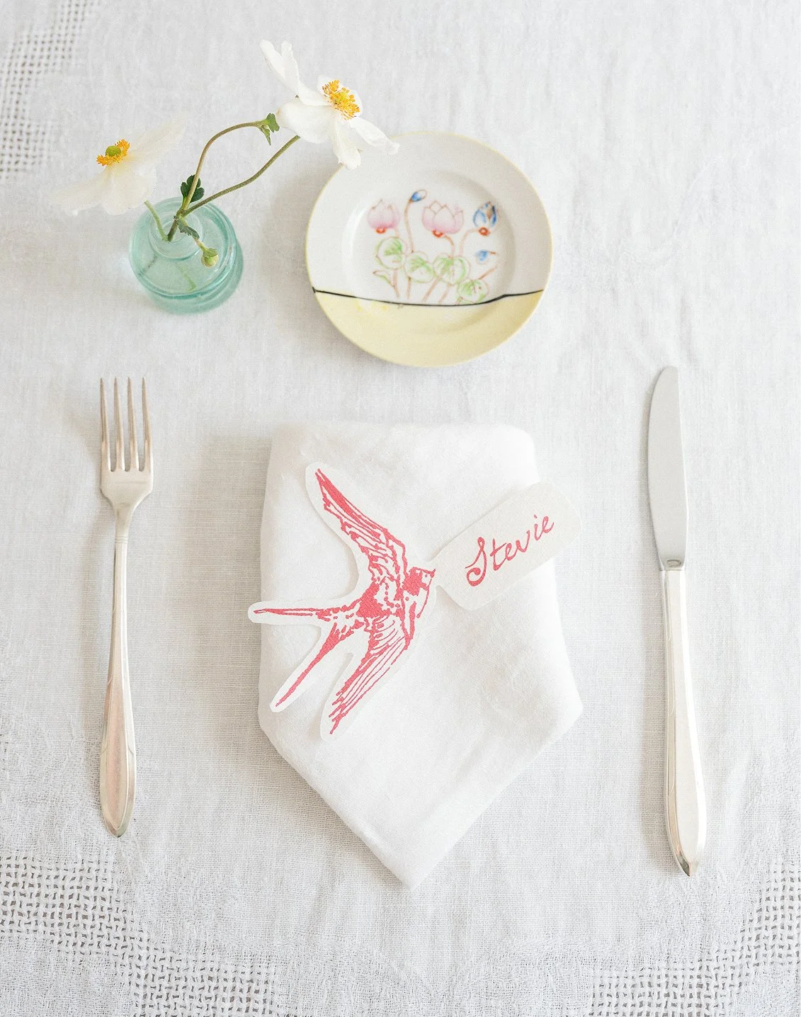 table set with swallow place card, small plate, napkin, utensils, and anemones 