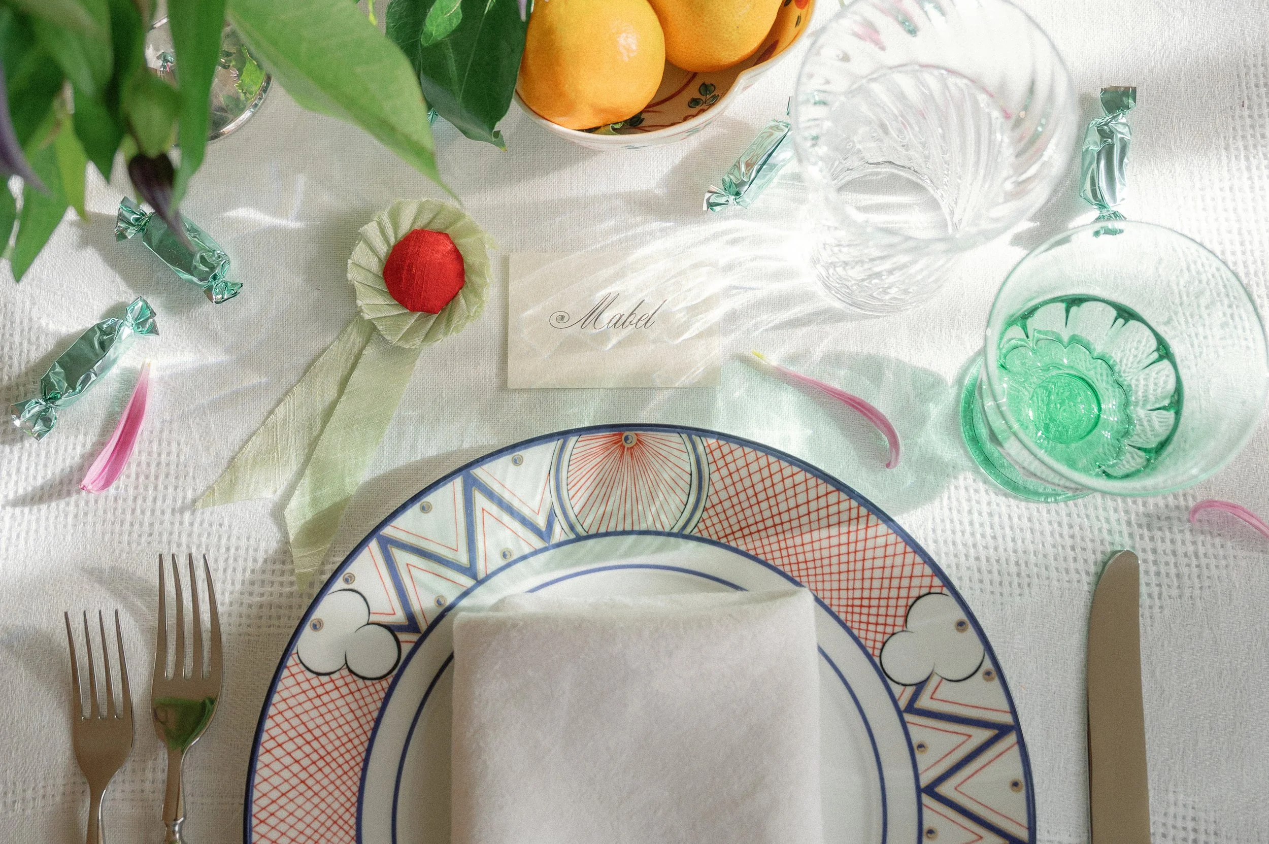 Table setting with Tiffany plate, silk award ribbon, pink petals, clematis, oranges, and place card setting