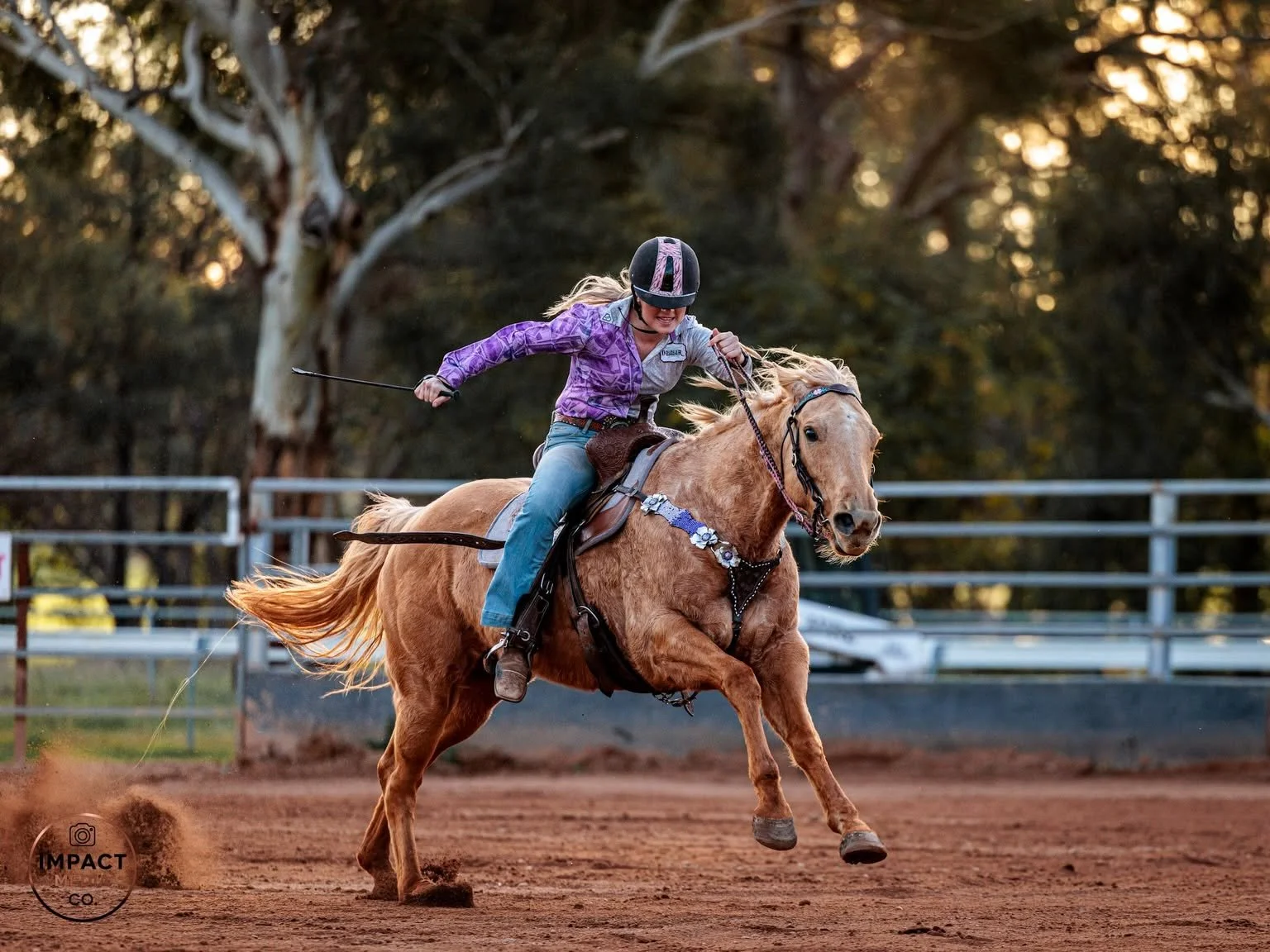 Barrel racer gallops a horse across a dirt arena at sunset.