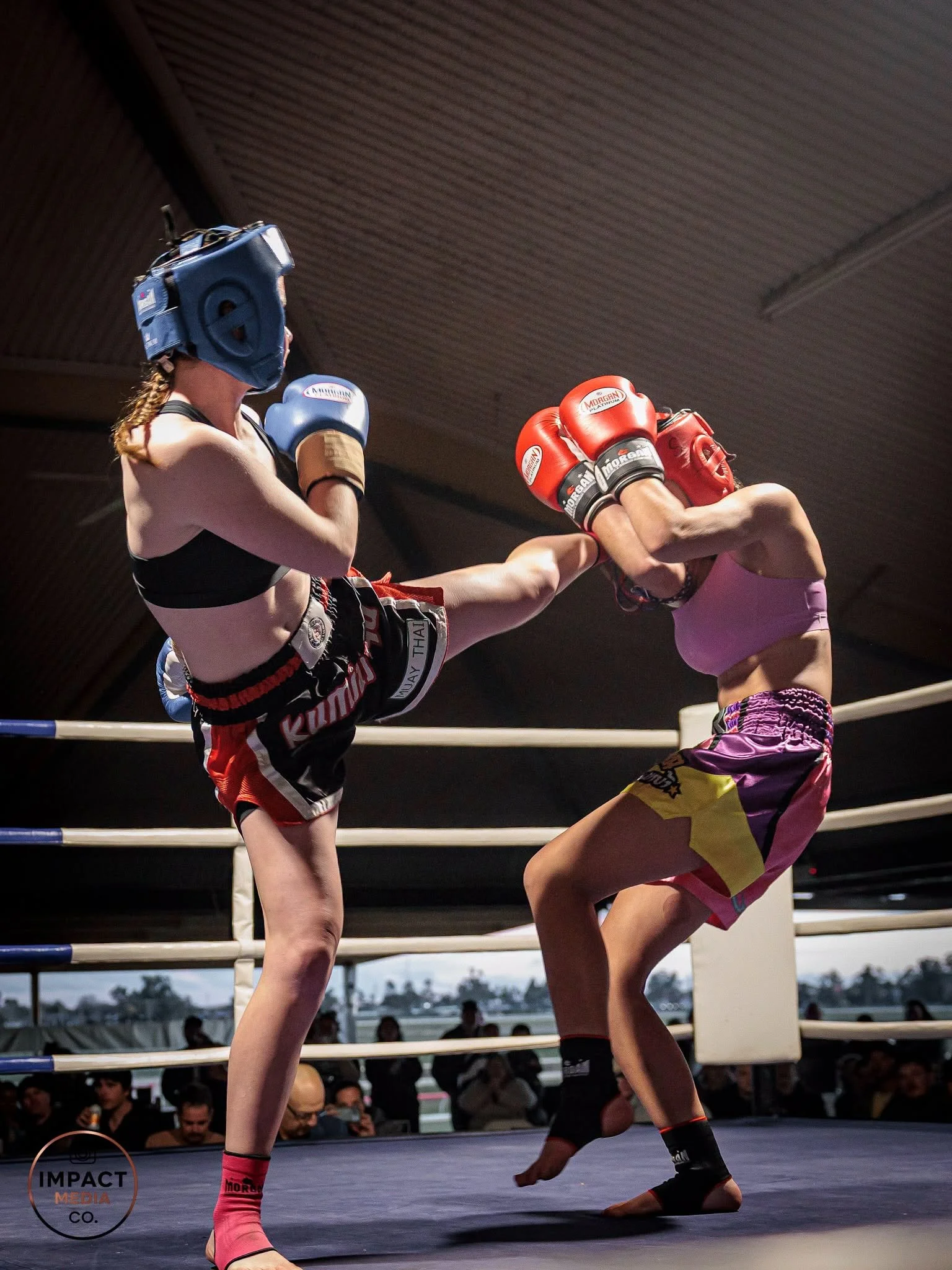 Two female Muay Thai fighters exchange kicks inside a boxing ring.