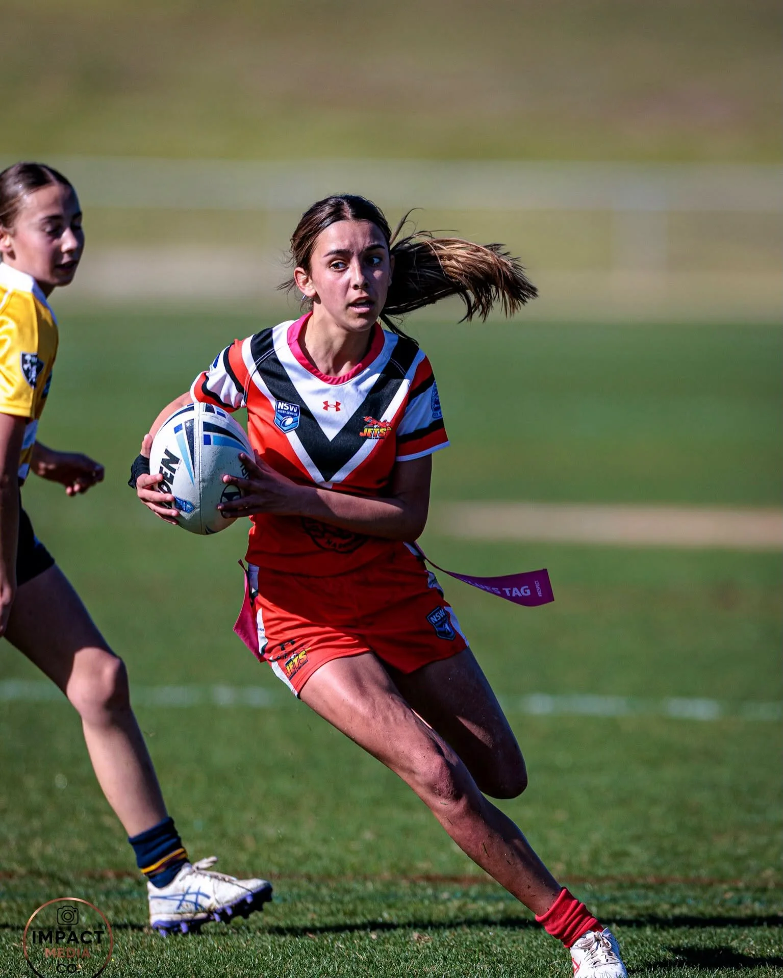 Female rugby league player in red and black runs with the ball during a match.