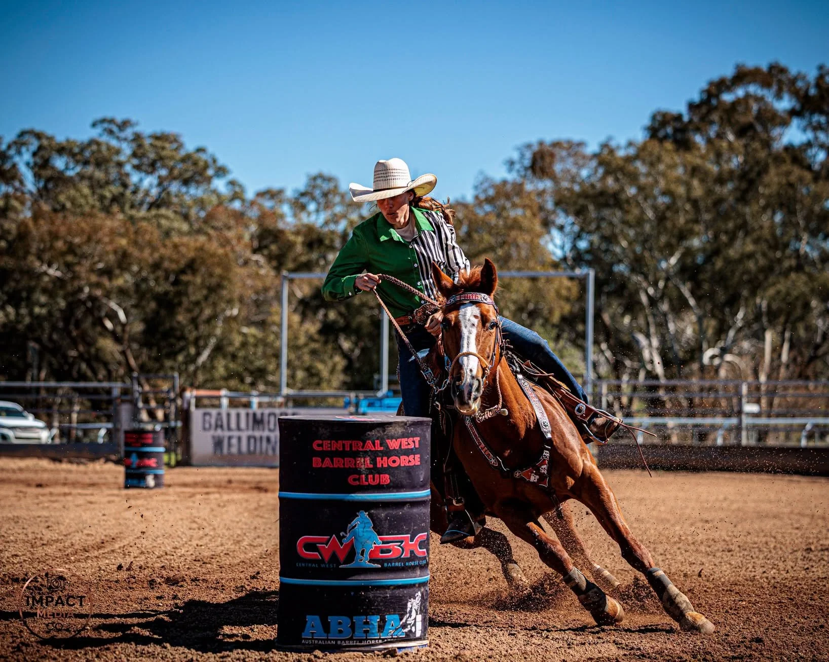 Barrel racer in a green shirt and white hat turns around a black barrel.