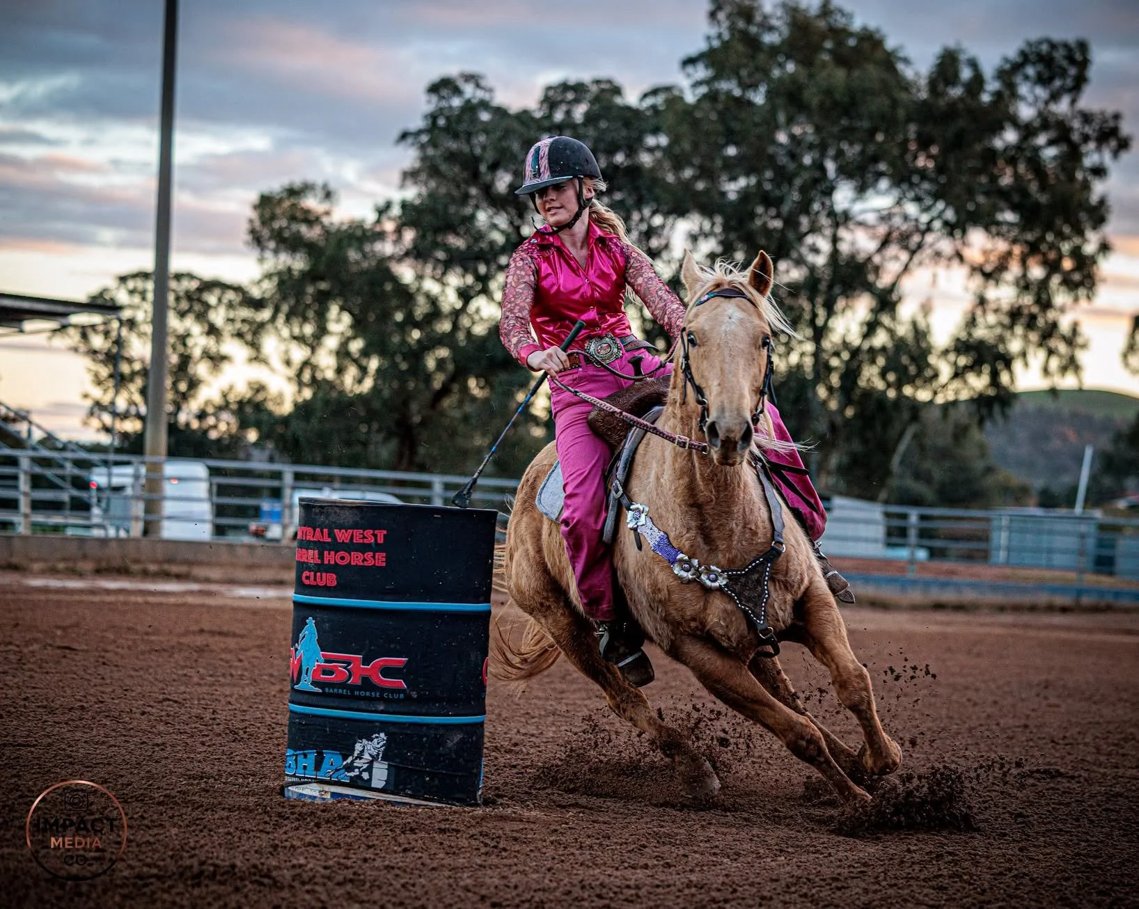 Barrel racer on a palomino turns a Central West Barrel Horse Club barrel at sunset.
