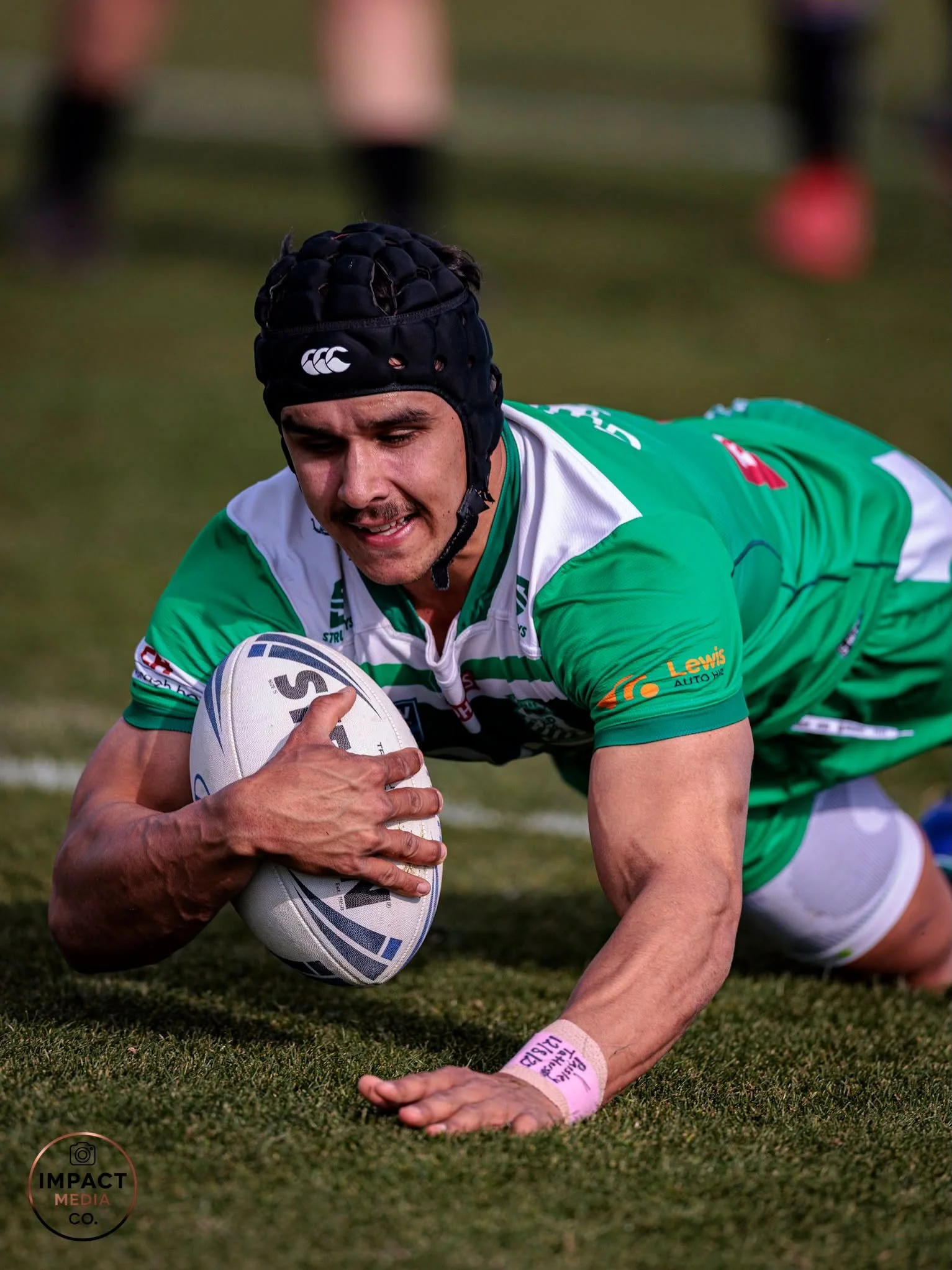 Rugby league player in green headgear holds the ball after a tackle.