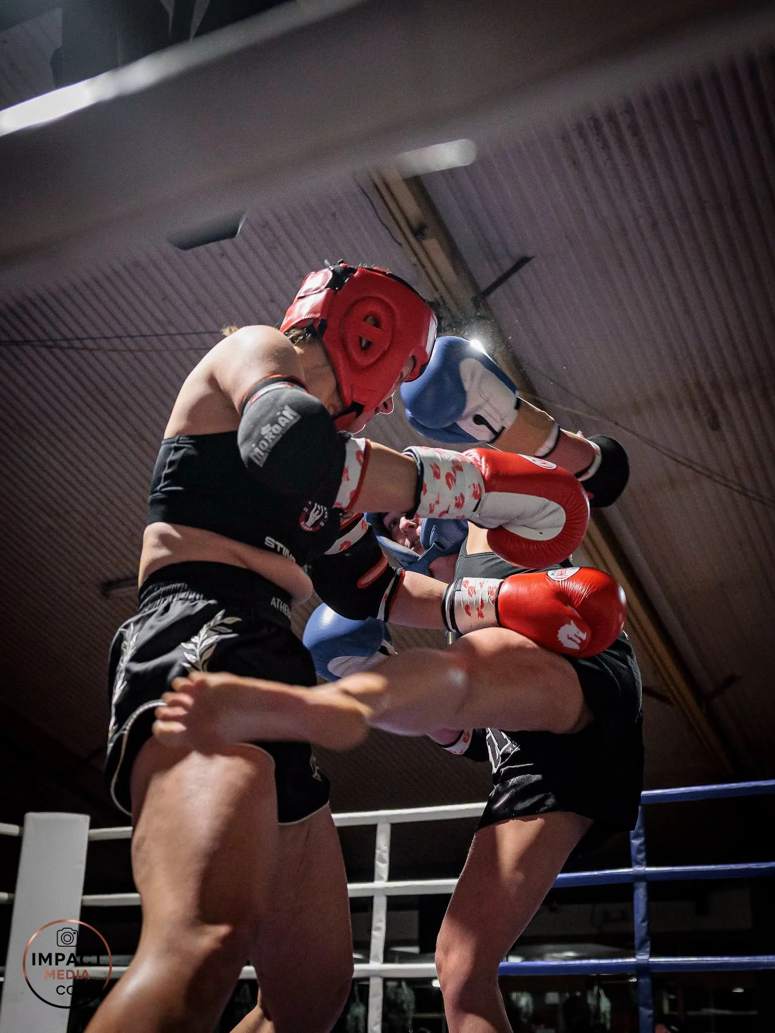 Two amateur boxers wearing protective headgear compete in the ring.
