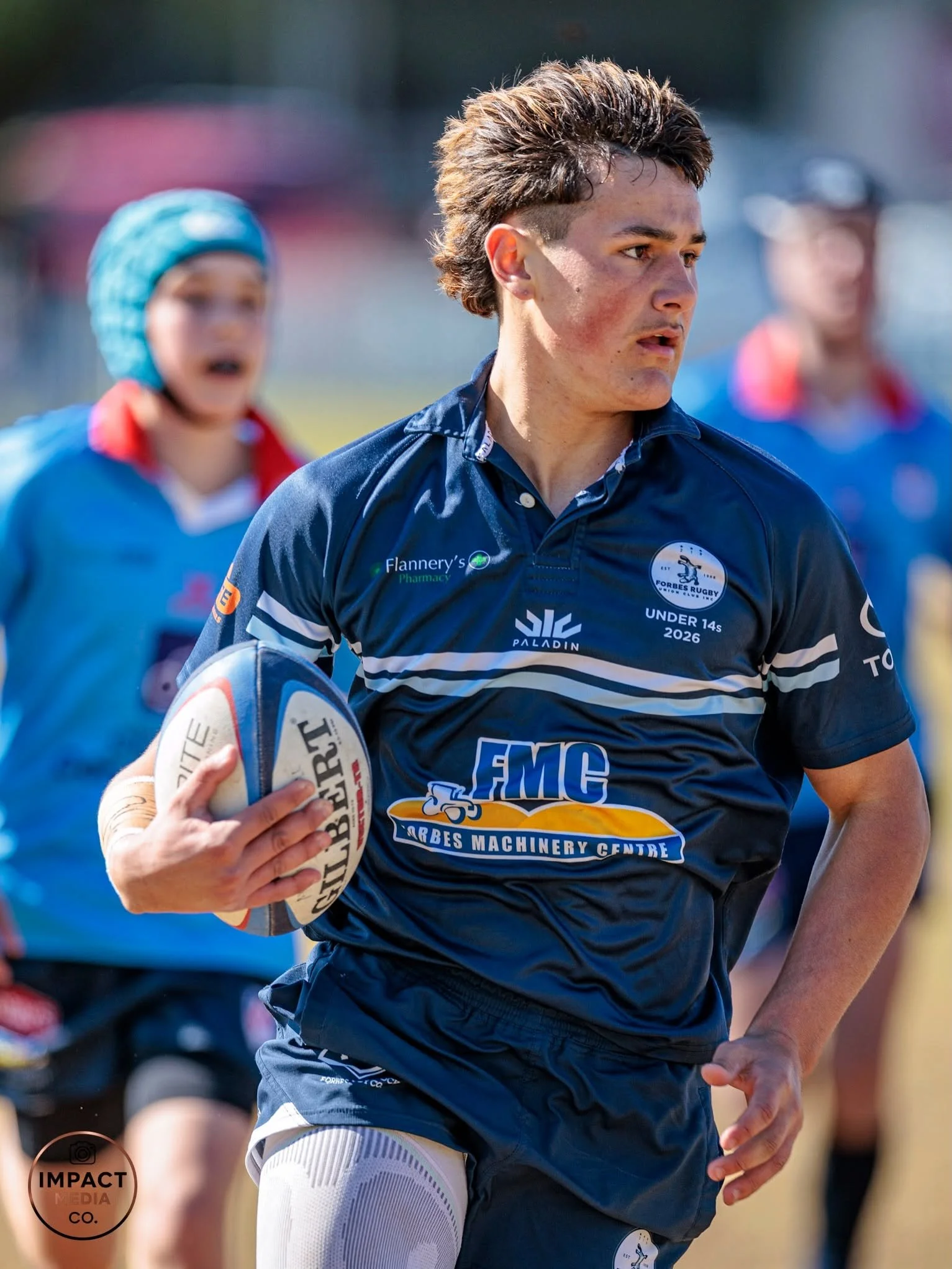 Junior rugby league player in blue holds the ball with teammates behind him.