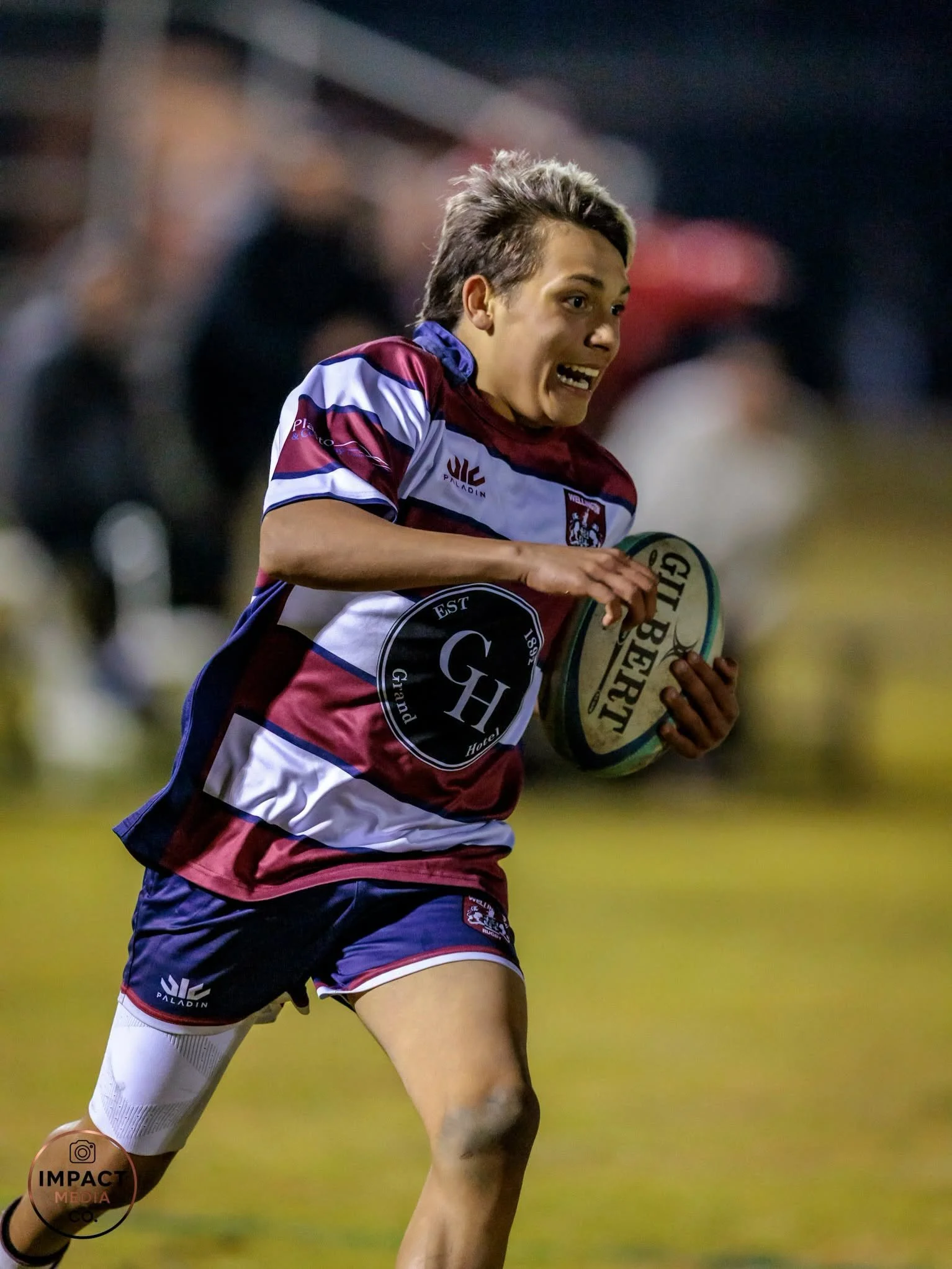 Female rugby league player in a maroon, white and navy jersey runs with the ball.