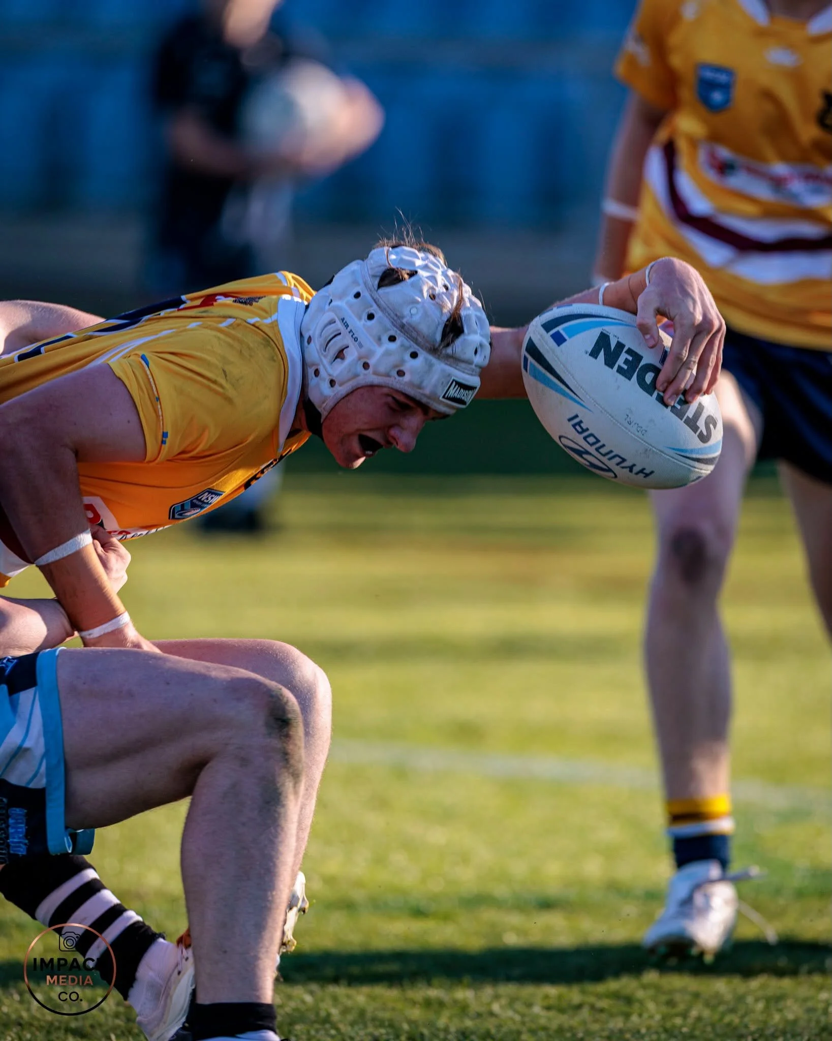 Rugby league player in a yellow jersey and white headgear holds the ball during a match.