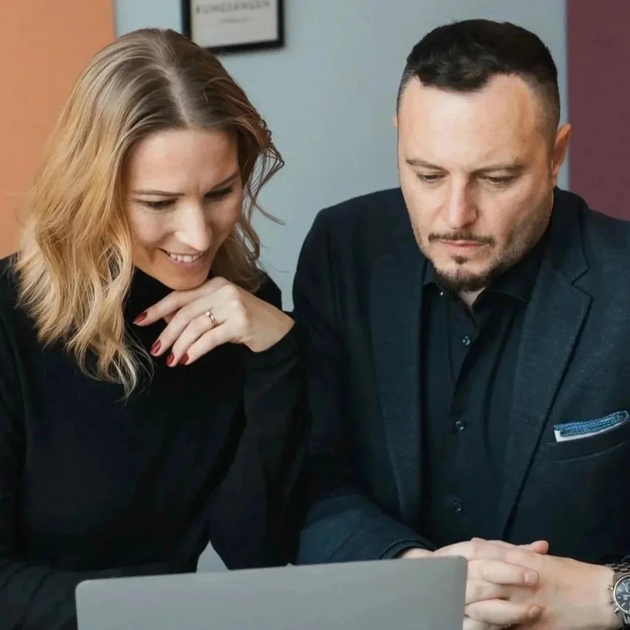 A woman and a man in professional attire looking at a laptop screen, engaged in a discussion.