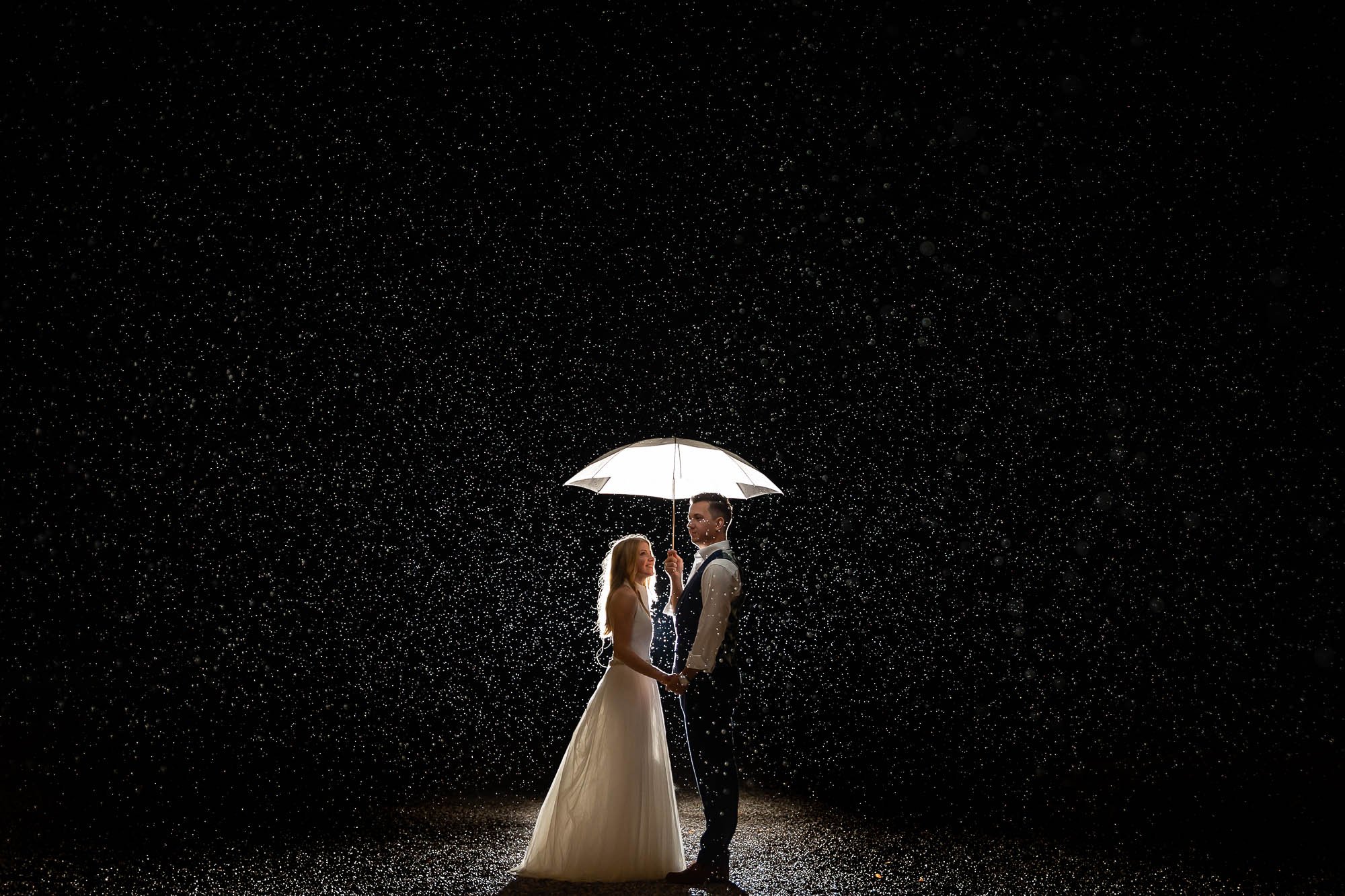 Bride and groom with umbrella in the rain at night