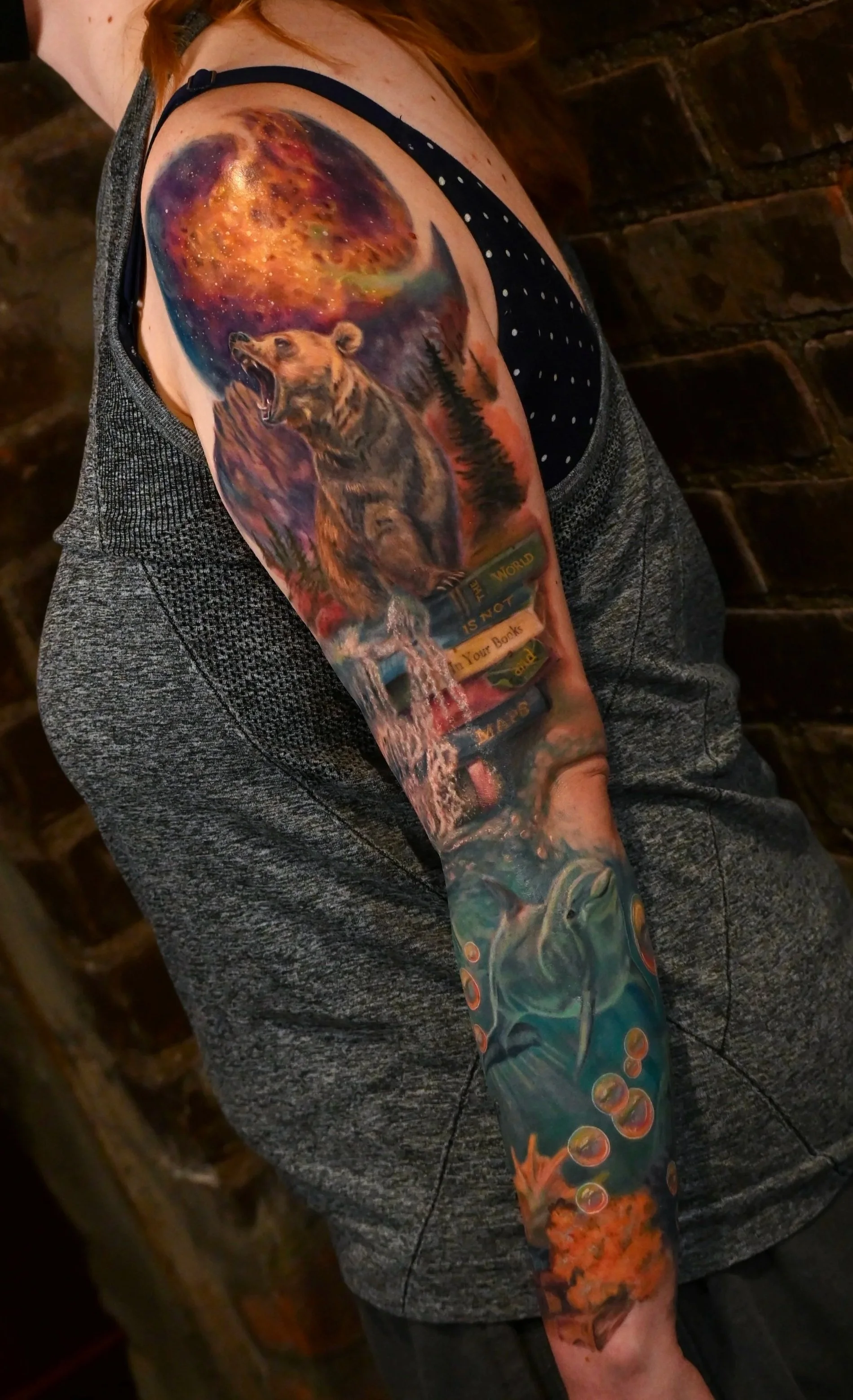 Colorful tattoo sleeve featuring a bear, a stary cosmic night sky, a waterfall, a dolphin, and underwater scenery.