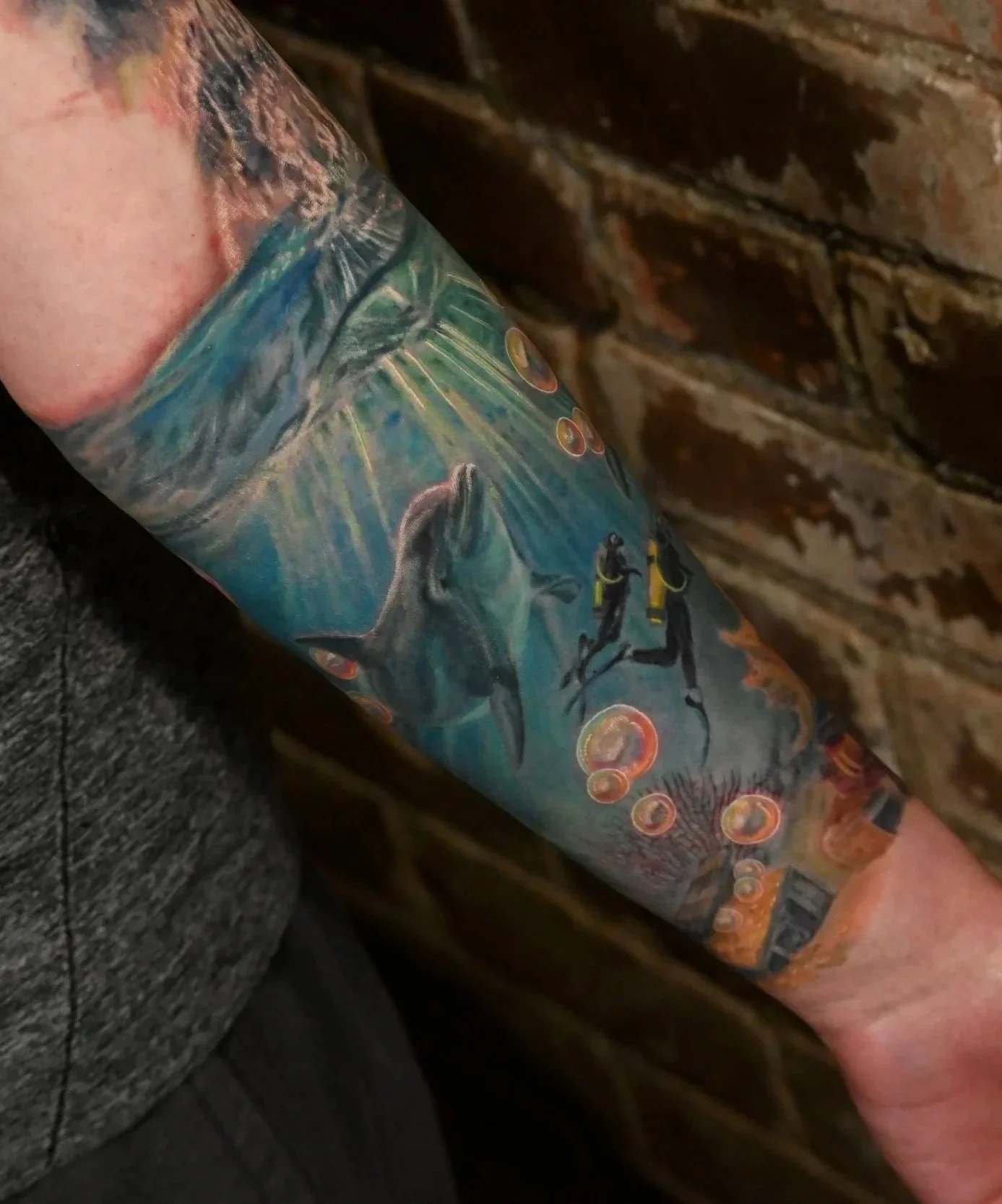 Colorful tattoo featuring a diver, dolphins, orange bubbles, and an underwater scene.