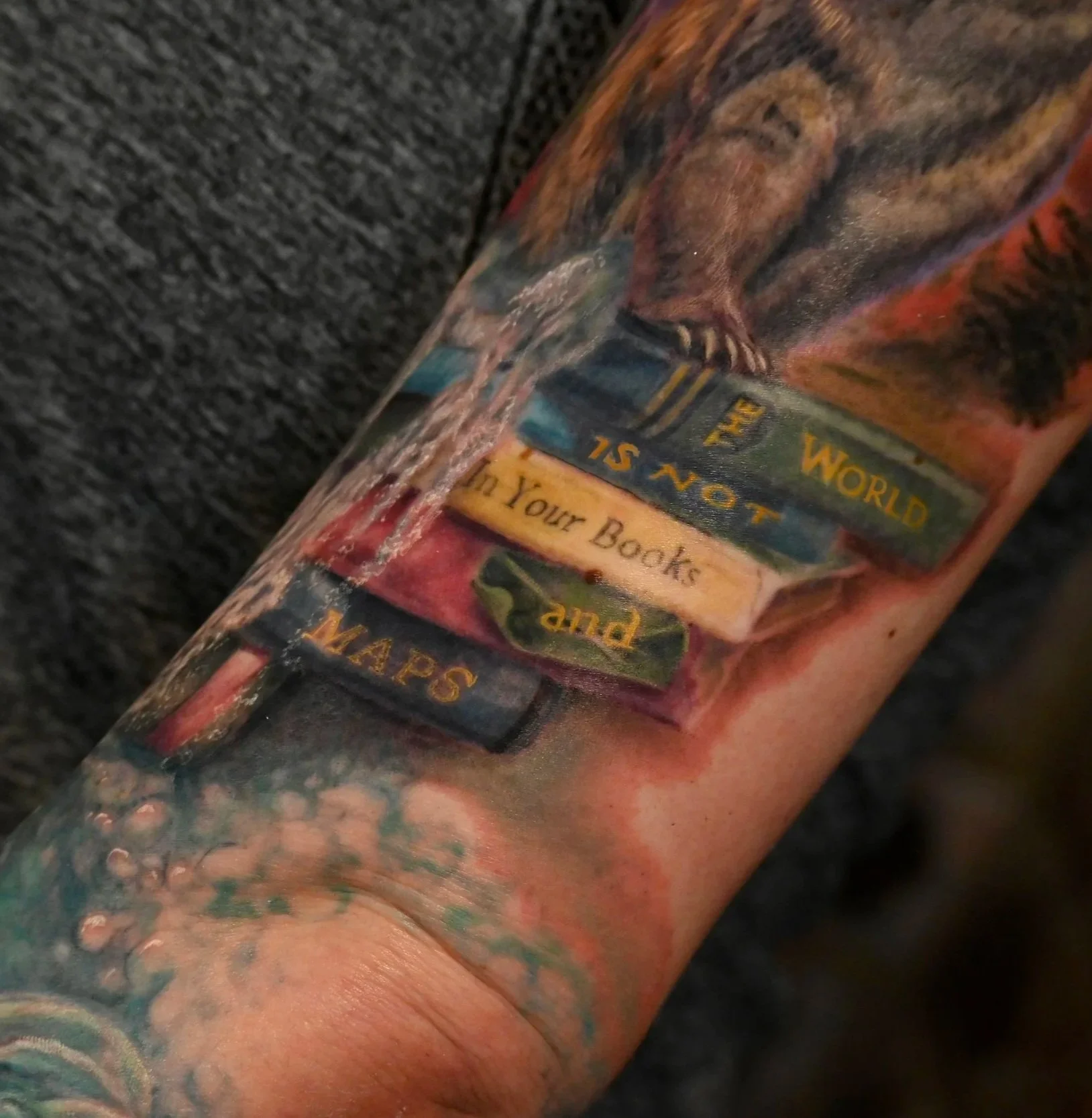 Tattoo of a stack of books titled 'The World Is Not Your Books and Maps' on a person's forearm.
