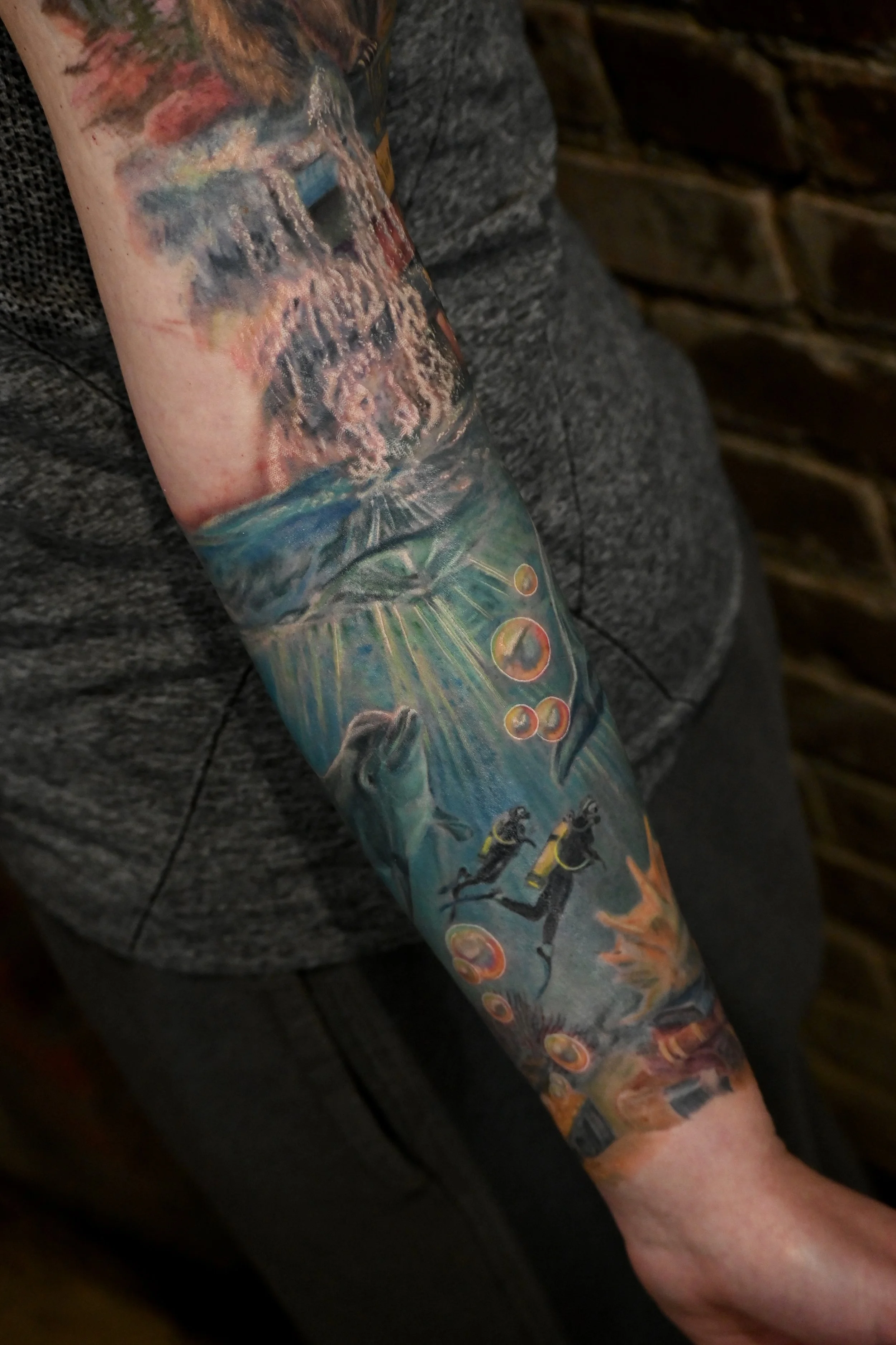 Tattoo of an underwater scene with divers, dolphins, a treasure chest, and books.