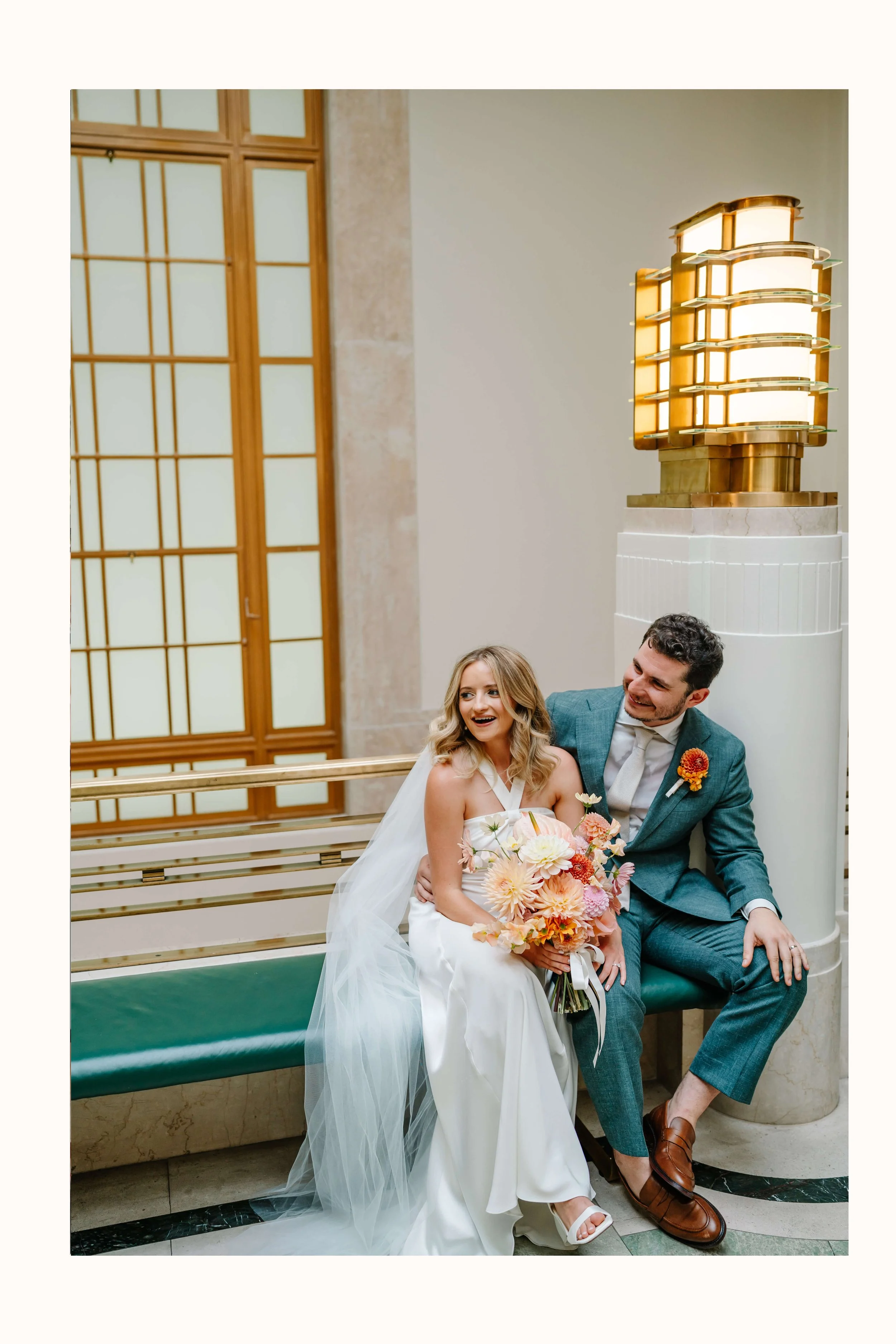 Wedding couple at Hackney Town Hall, sitting inside on art deco bench waiting for confetti