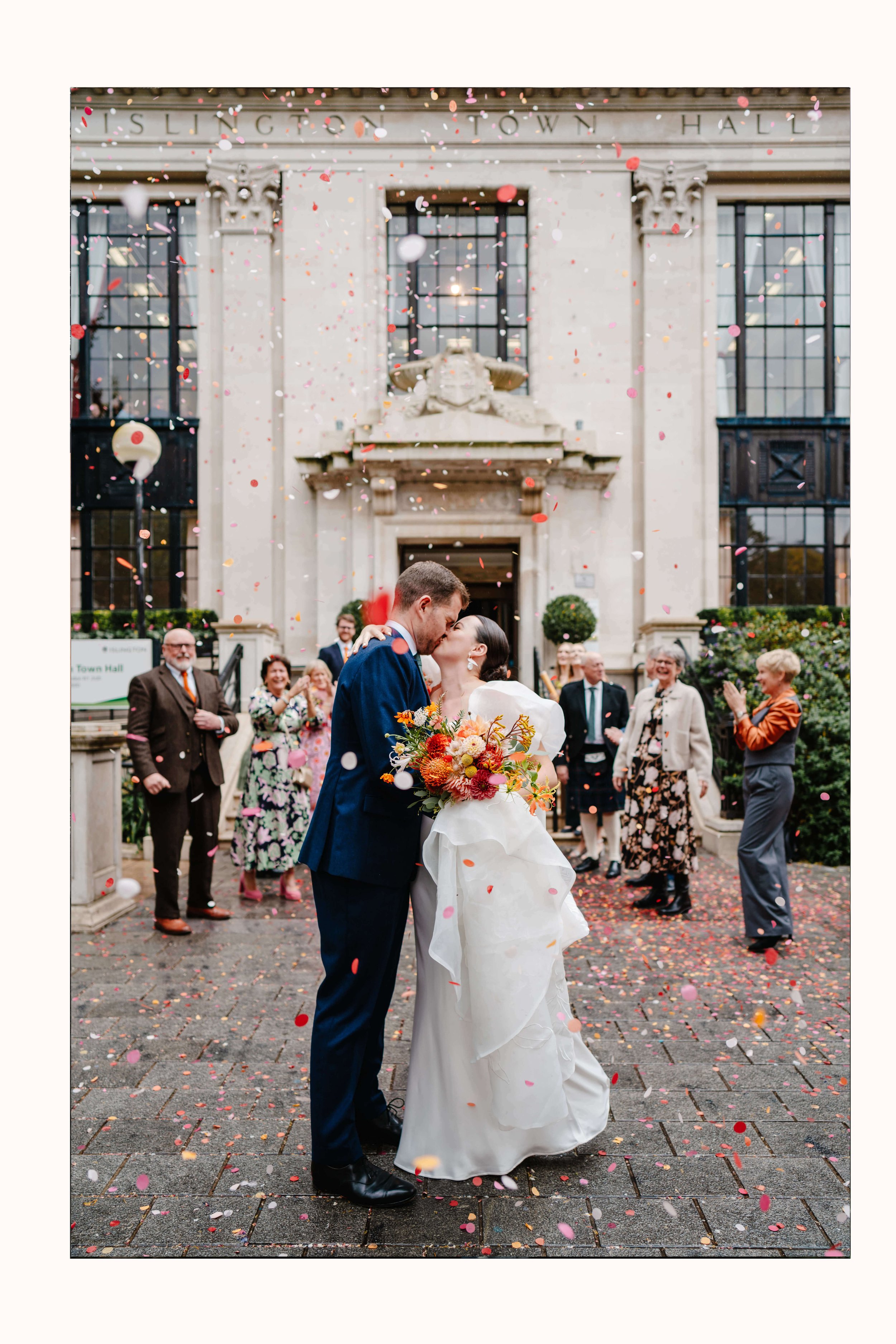 Wedding photo at Islington Town Hall, couple kiss during confetti throw