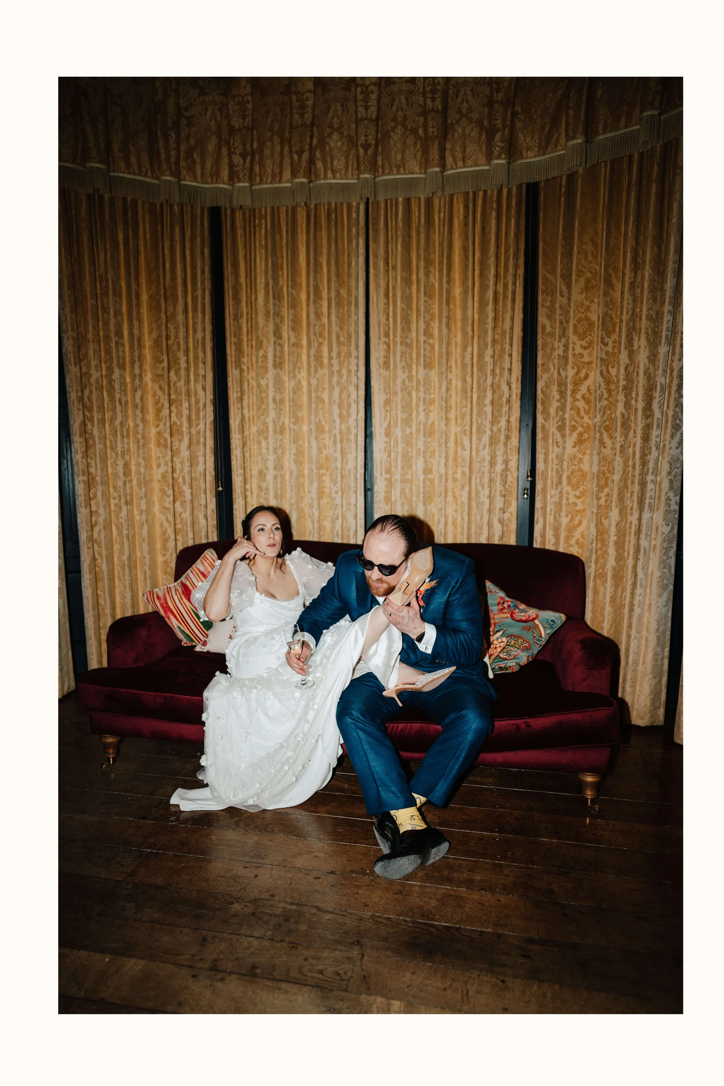Bride & Groom sitting on sofas at Elmore Court, having a fun playful moment. Wedding Photos using flash photography