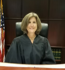Woman in judge robe sitting at bench with USA flag