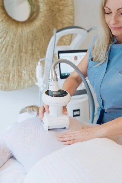 A woman receives a body contouring treatment with a handheld device in a spa or clinic setting.
