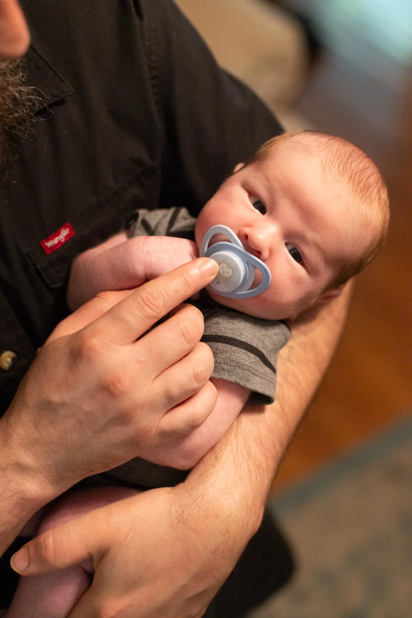 A person holding a baby with a pacifier in its mouth, the baby's head resting on the person's arm, and the person's hand gently supporting the baby's head.