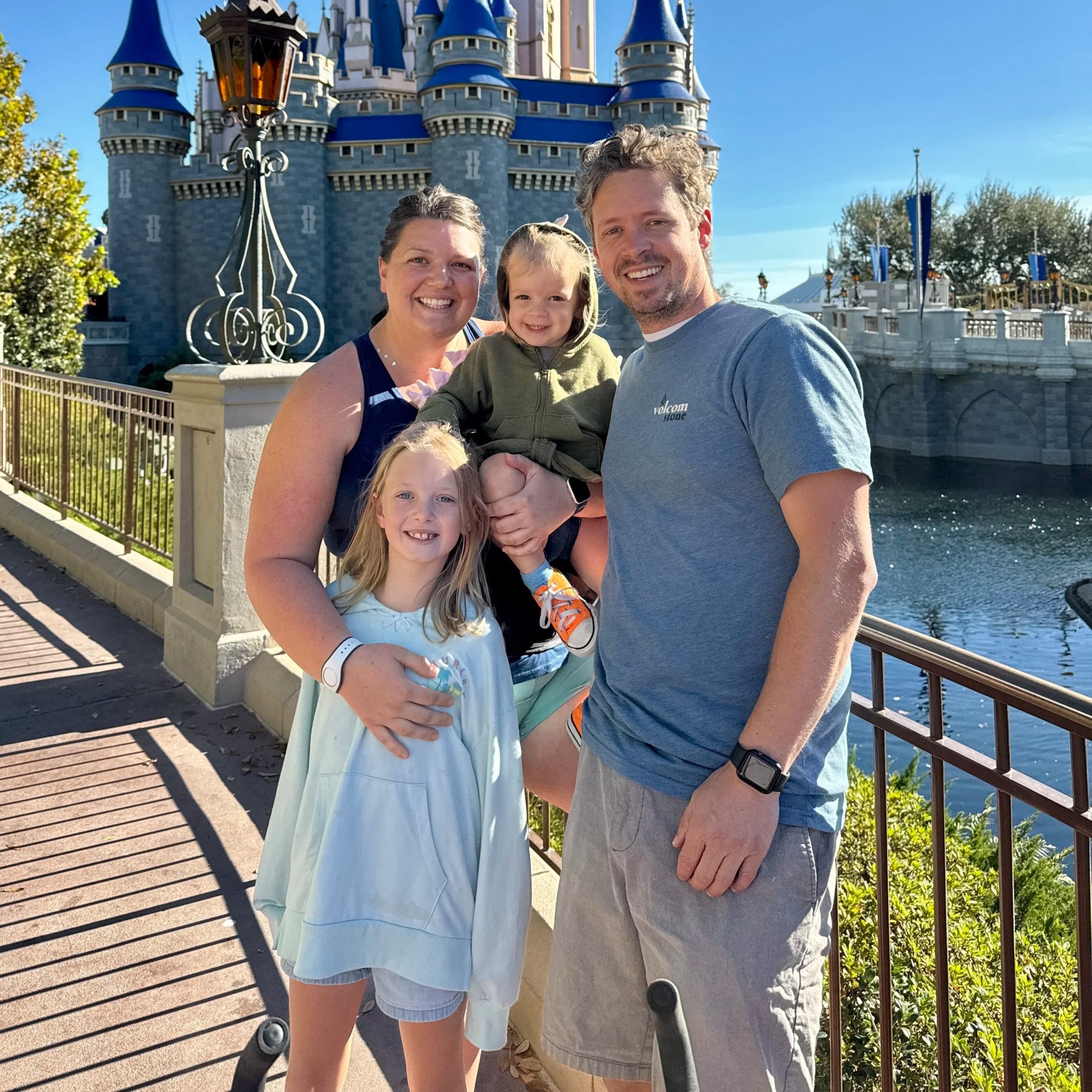 A smiling family of four posing in front of Sleeping Beauty Castle at Disneyland.