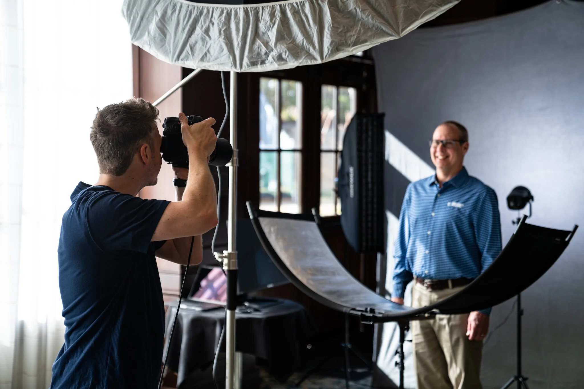 Photographer taking a professional headshot shot photo of a man in a photography studio with lighting equipment and a backdrop.