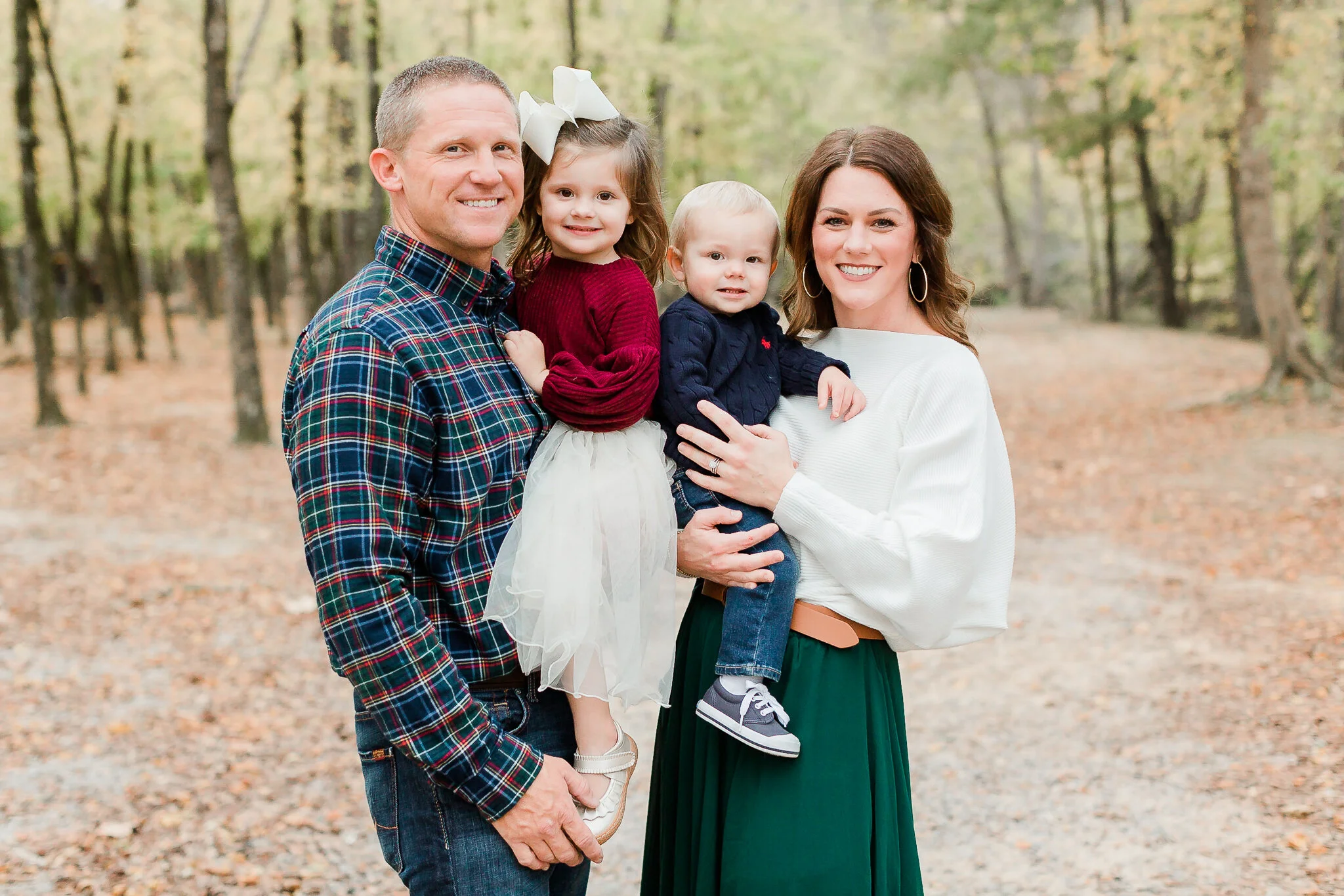 Family of four with a man, woman, and two children standing in a wooded area, all smiling.