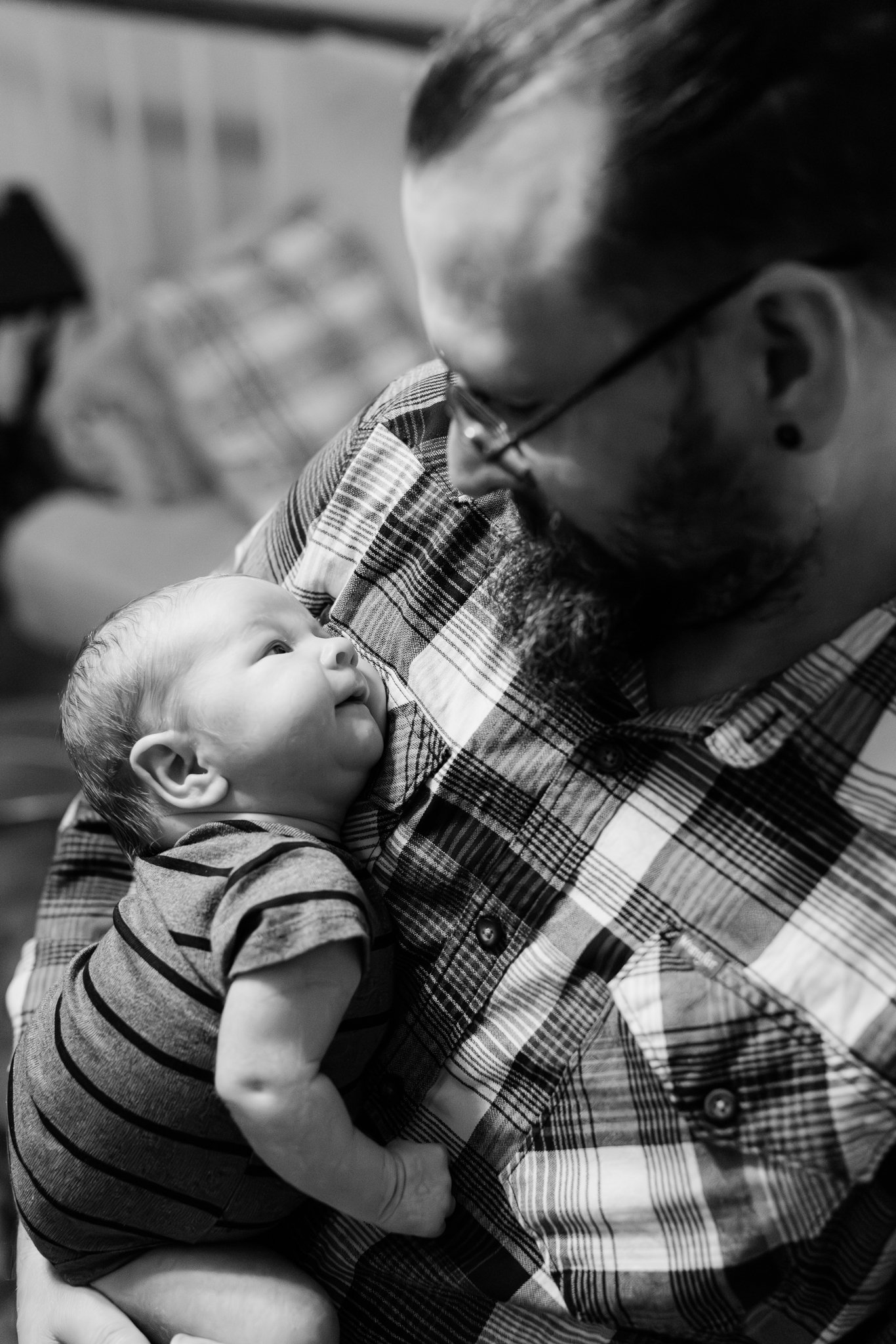 A man with glasses and a beard holding a young child with light hair in his arms, both looking at each other affectionately.