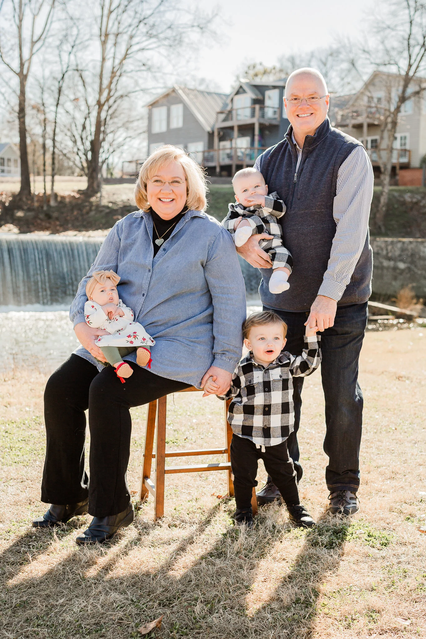 Family photo with an older couple and three young children, outdoors with houses and a waterfall in the background.