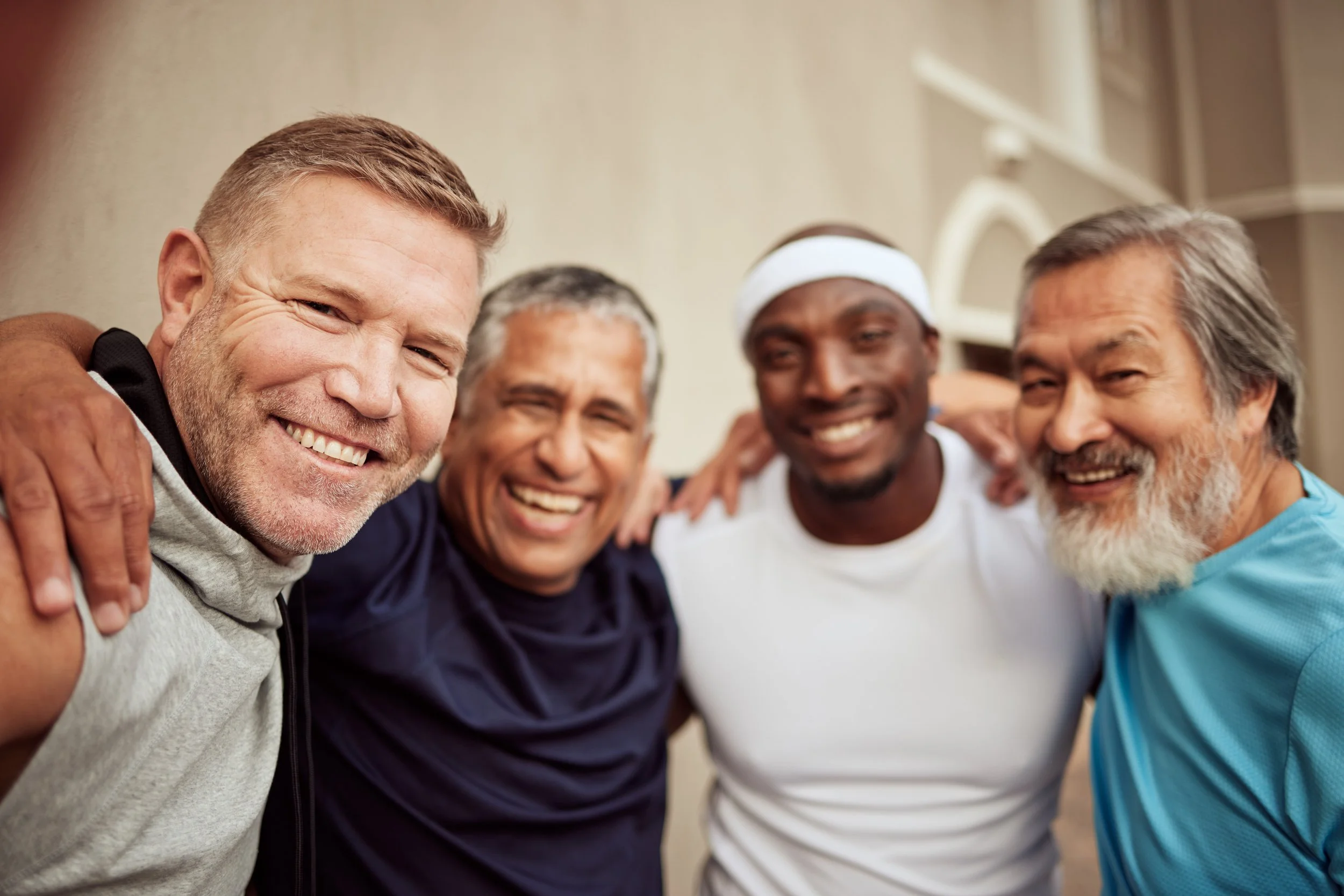 A group of five diverse men smiling and hugging each other in a close circle, celebrating friendship.