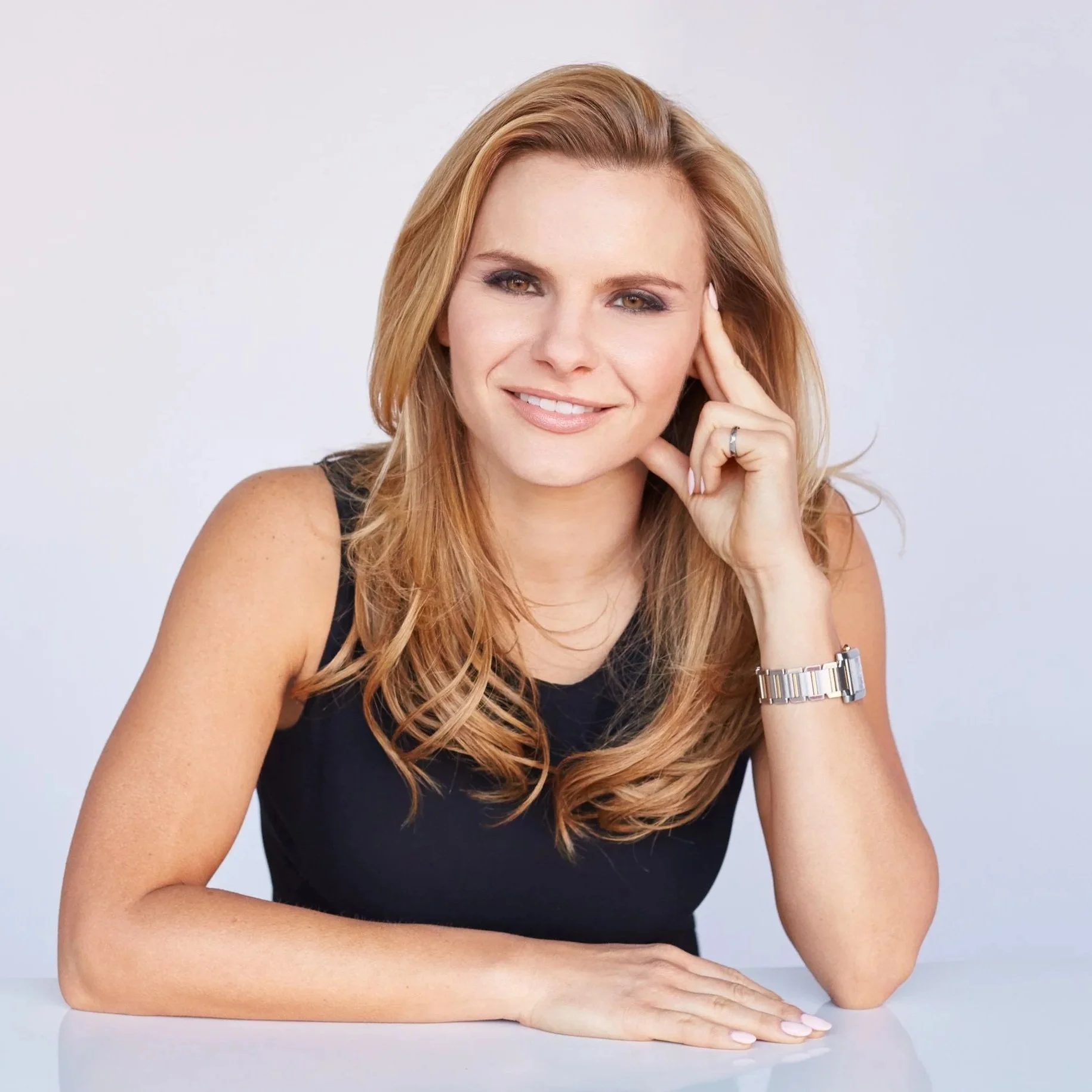 Woman with shoulder-length hair leans on her hand against a table