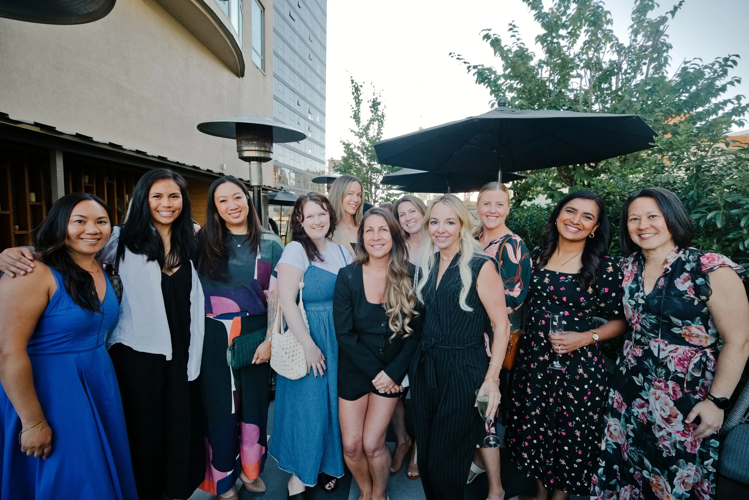 A group of smiling women are standing together on a rooftop