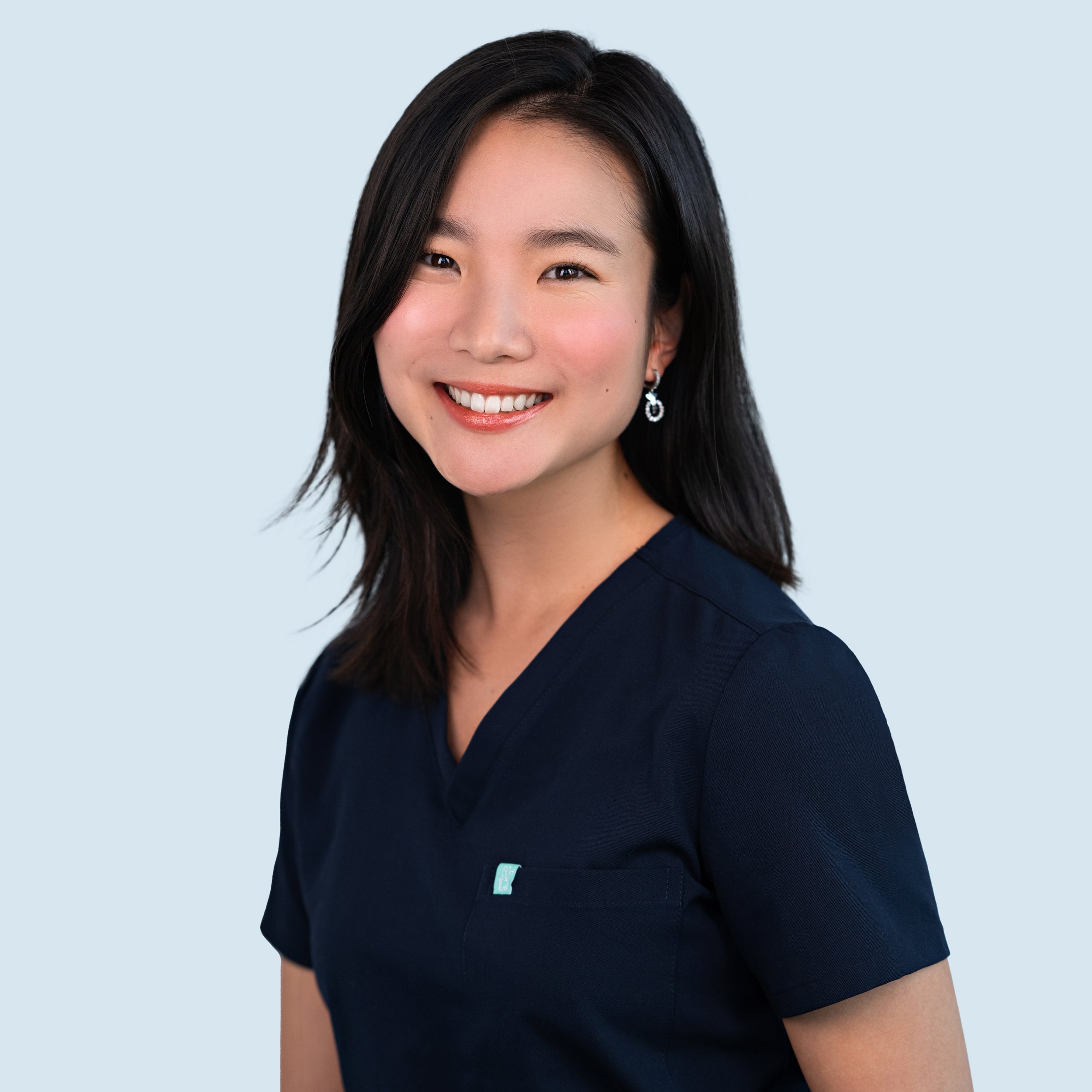 A smilng woman with straight dark hair and navy scrubs