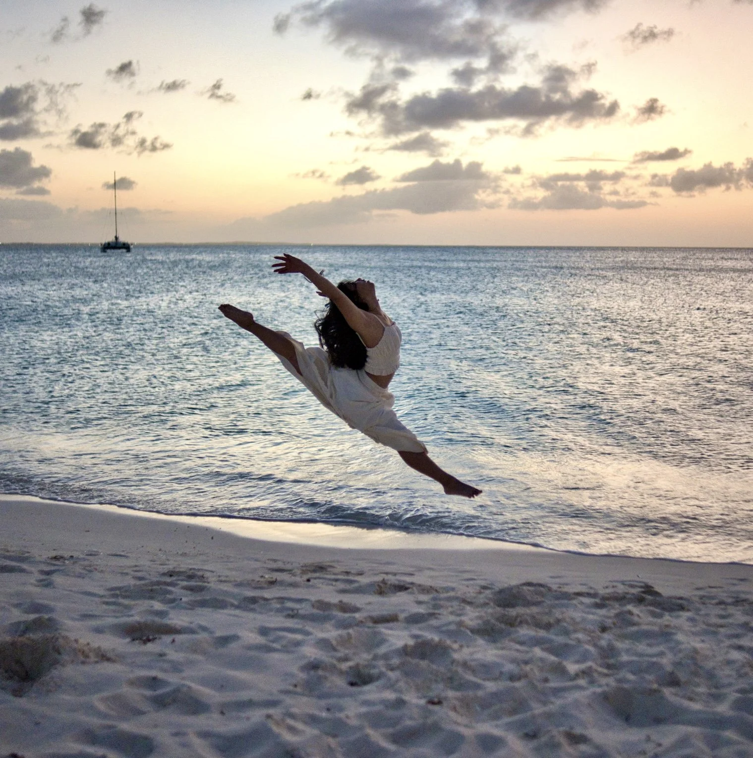 asian american teen aerial dancing on the beach in white clothes with sunset behind them