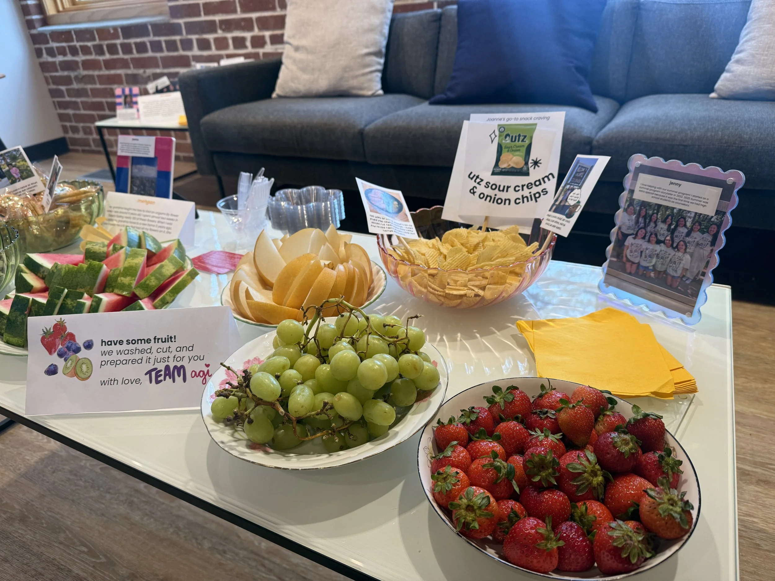  Plates of fresh cut watermelon, pears, strawberries, and grapes, and bowl of chips on table 