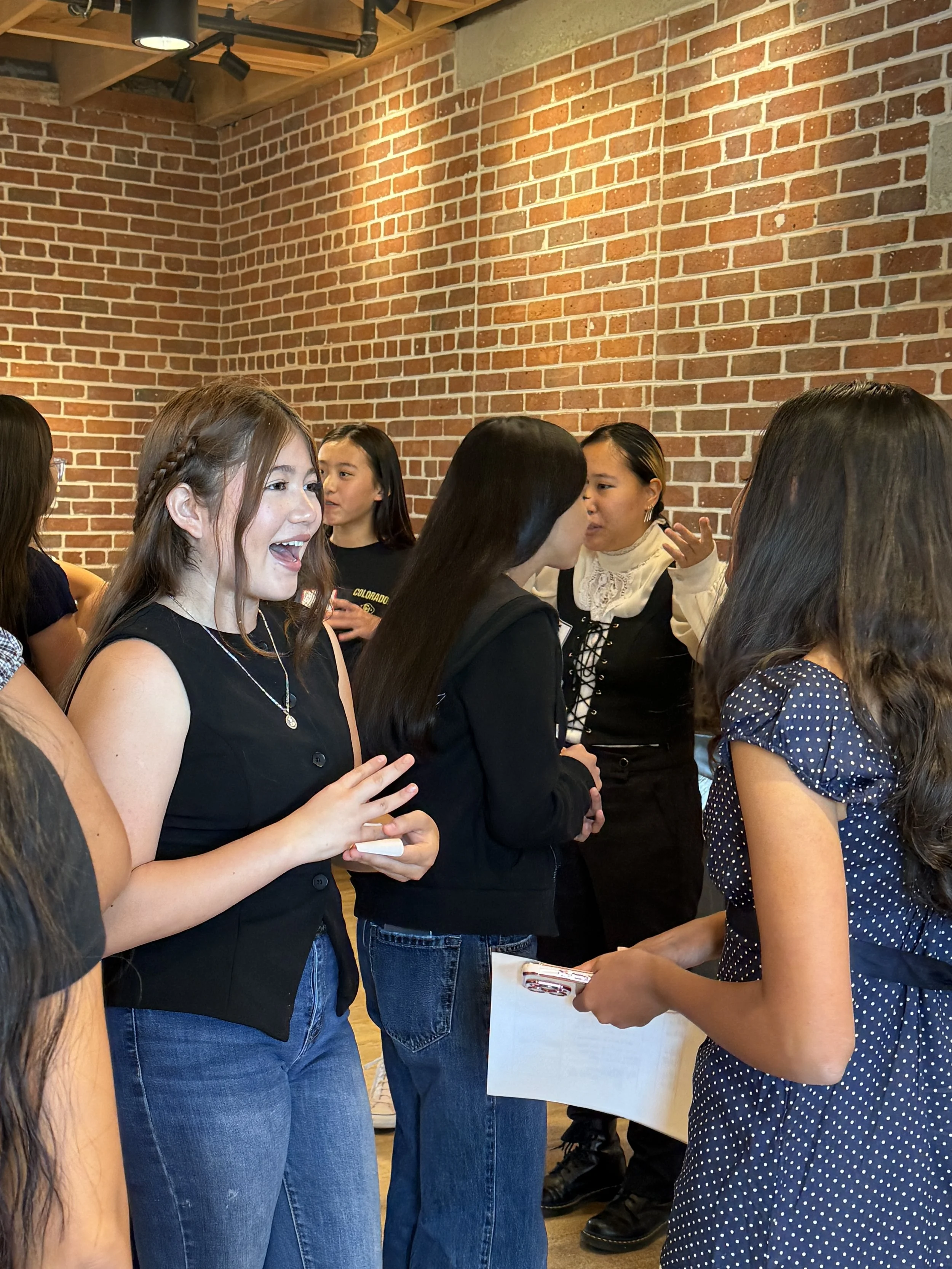  Student pairs conversating within a group of others; brick wall in background 