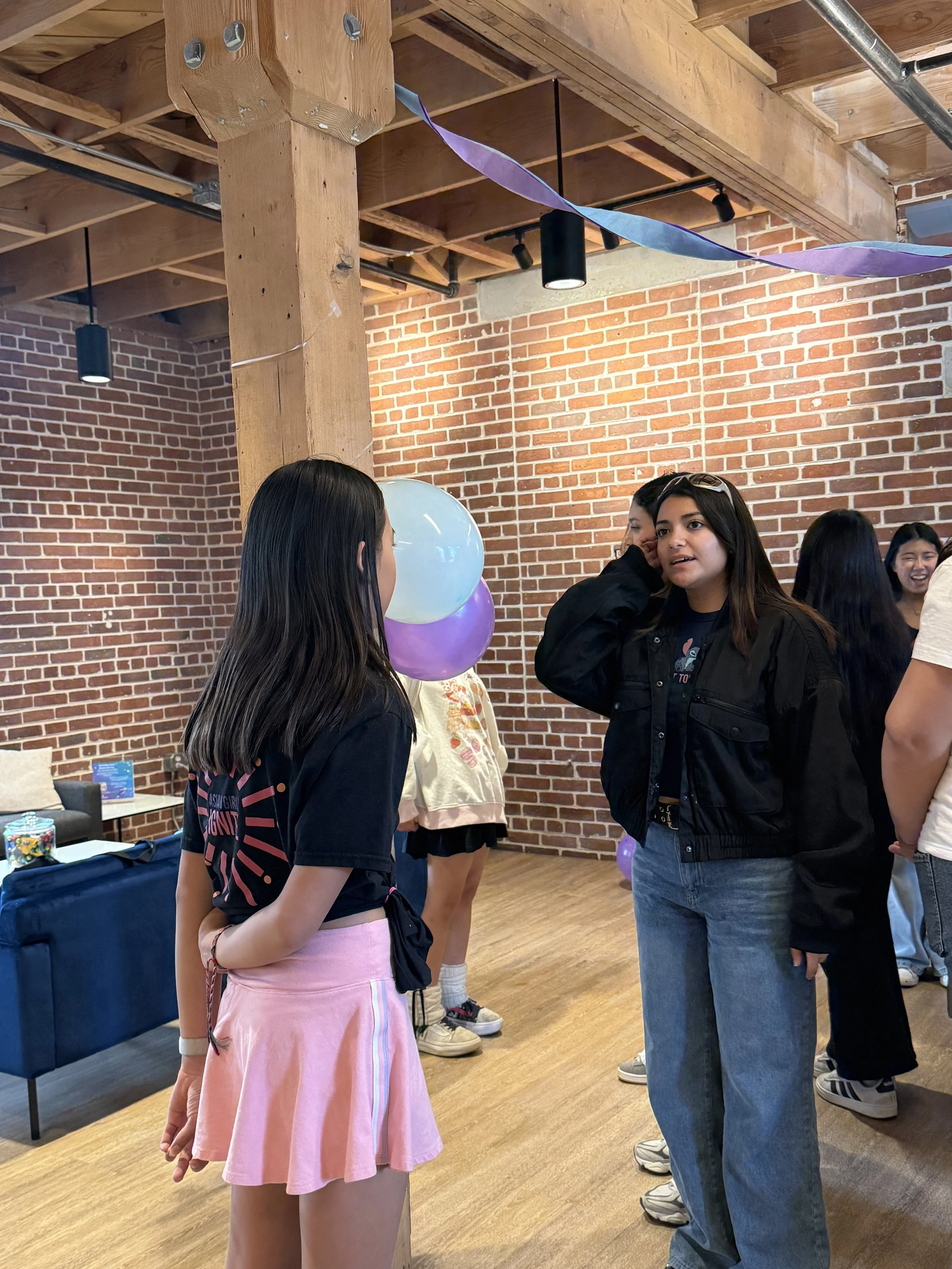  Student pairs conversating within a group of others; brick wall in background 