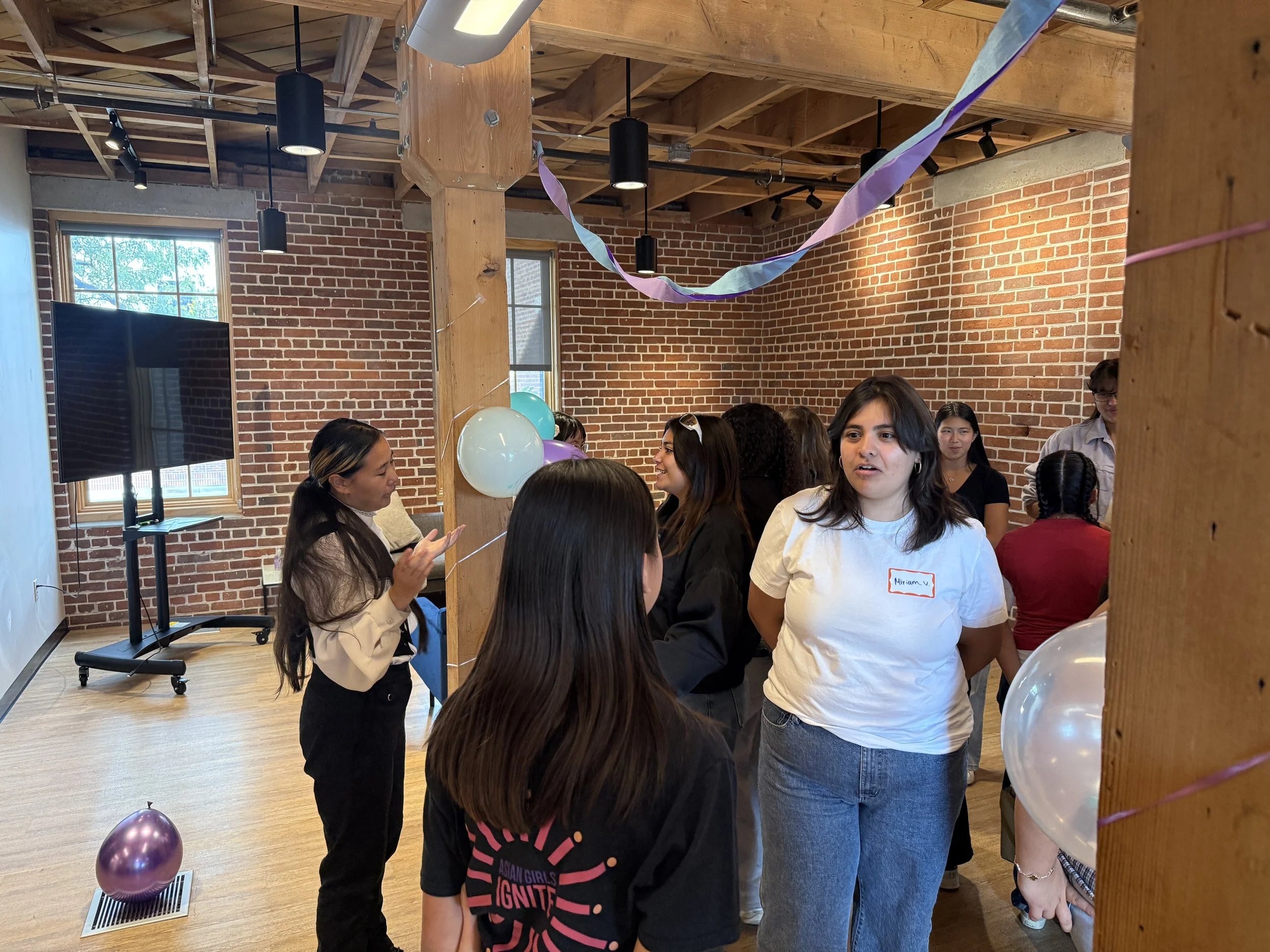  Student pairs conversating within a group of others; brick wall in background 