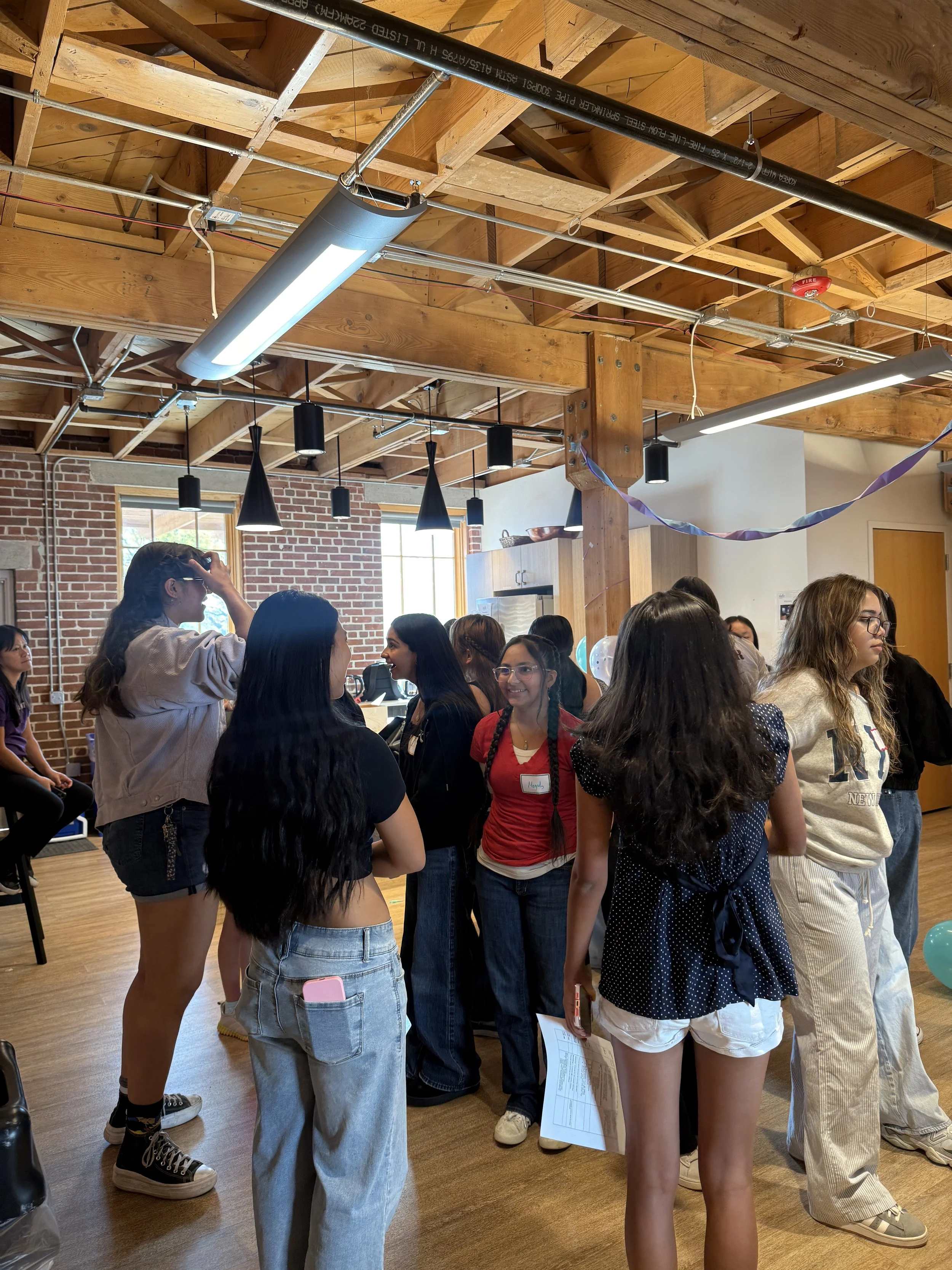  Student pairs conversating within a group of others; brick wall in background 