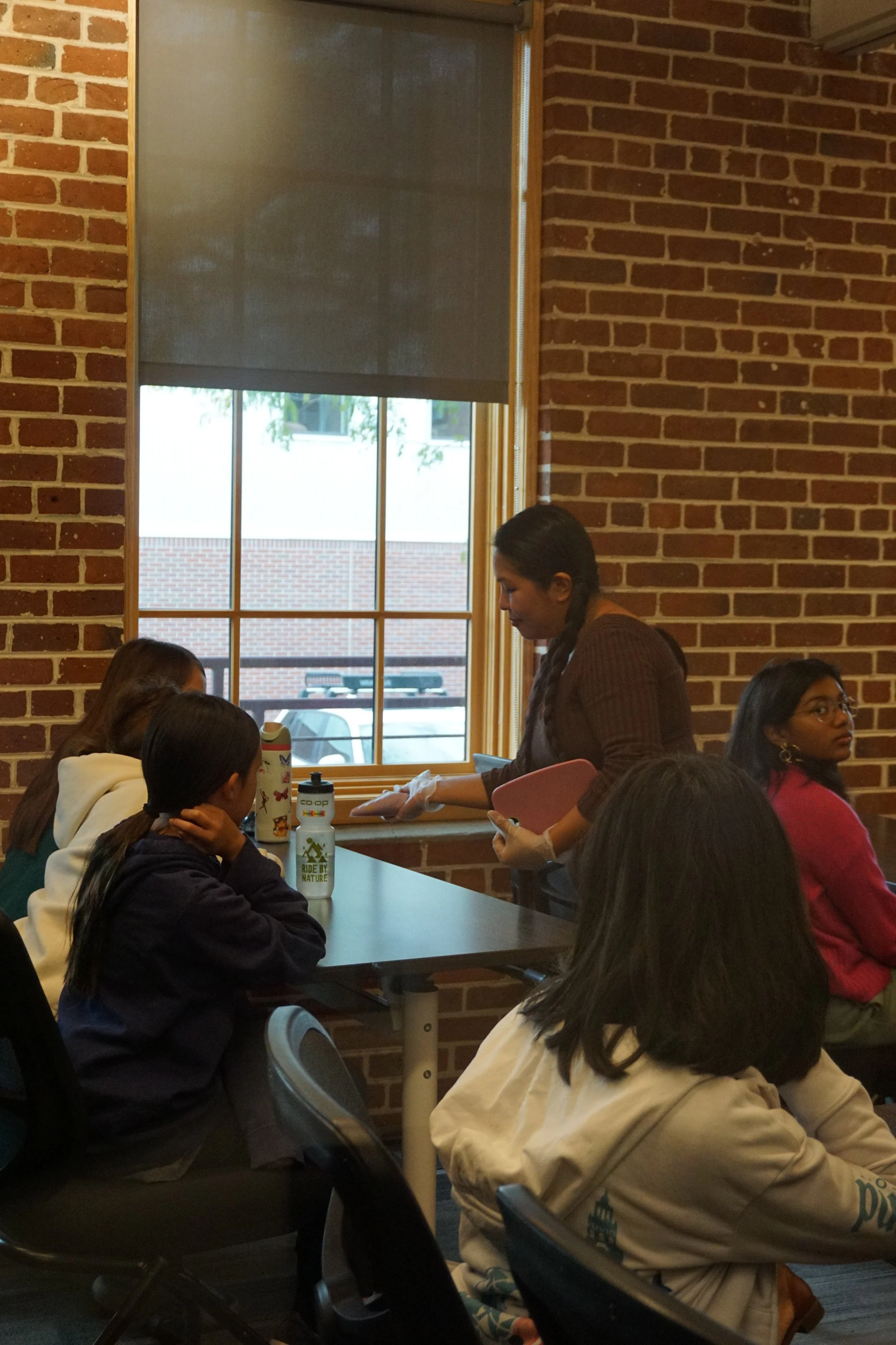  Thoa Nguyen completing a demonstration with icing amongst classroom with students; brick walls, long vertical window 