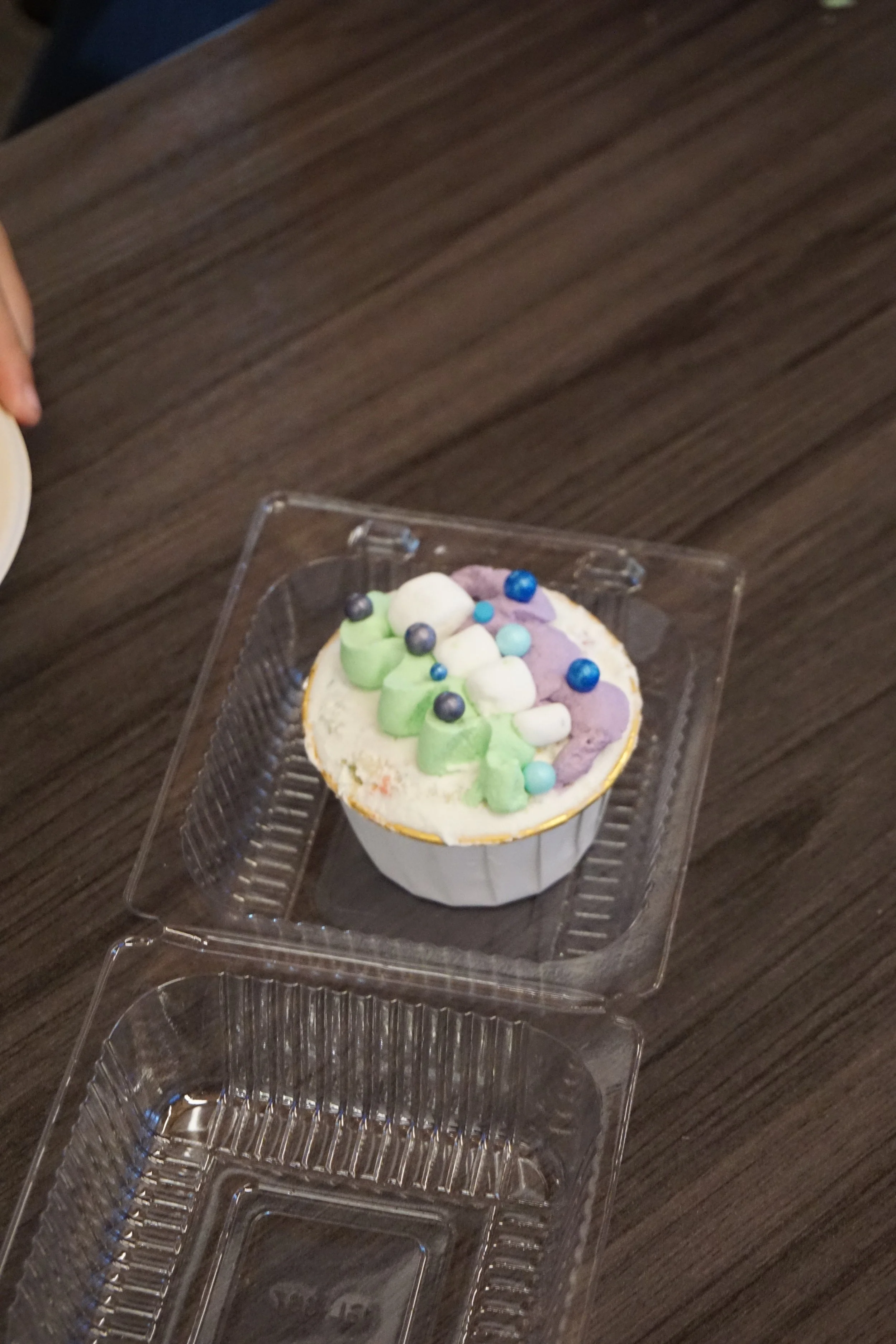  Cake cup with purple, white, and green frosting placed in a plastic square container 