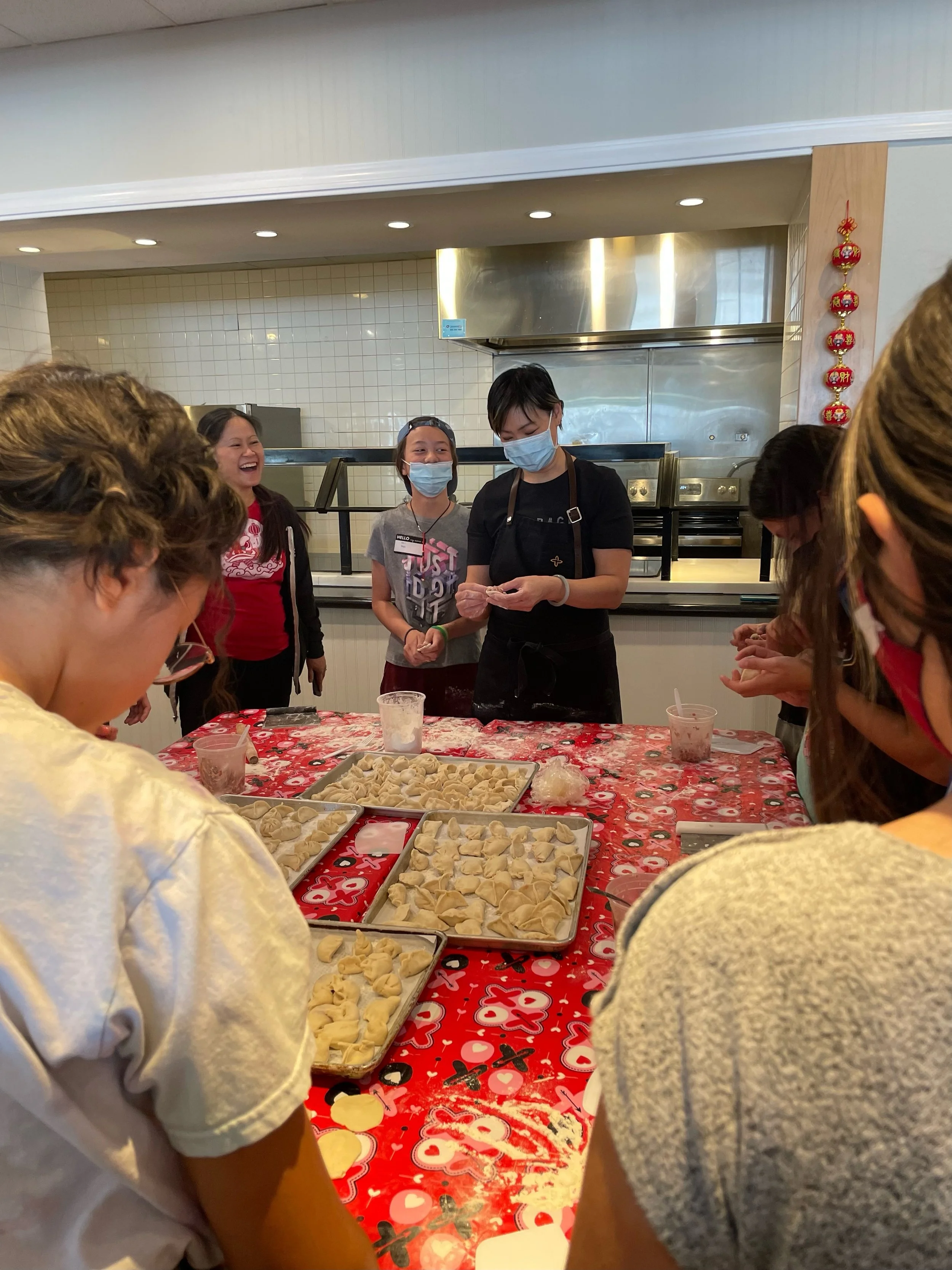 Chef Penelope Wong of Yuan Wonton demonstrating dumpling folding to students at a red decorated table at AGI Dumpling Making Workshop 2022