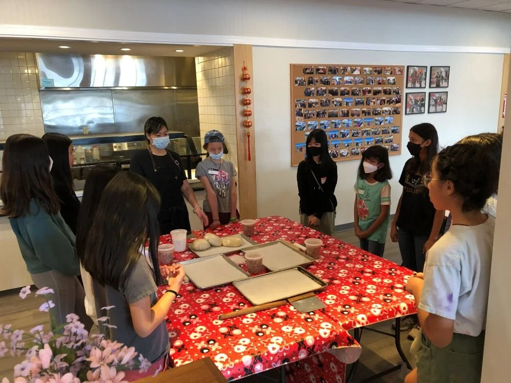 Chef Penelope Wong of Yuan Wonton demonstrating dumpling folding to students at a red decorated table at AGI Dumpling Making Workshop 2022