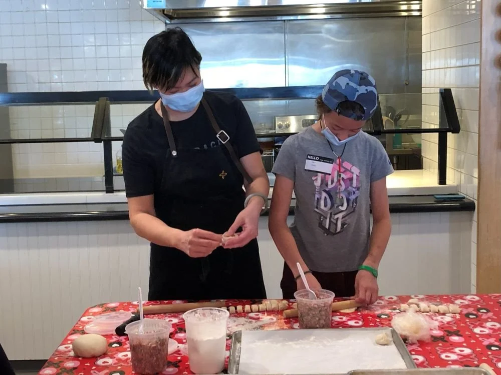 Chef Penelope Wong of Yuan Wonton demonstrating dumpling folding to students at a red decorated table at AGI Dumpling Making Workshop 2022