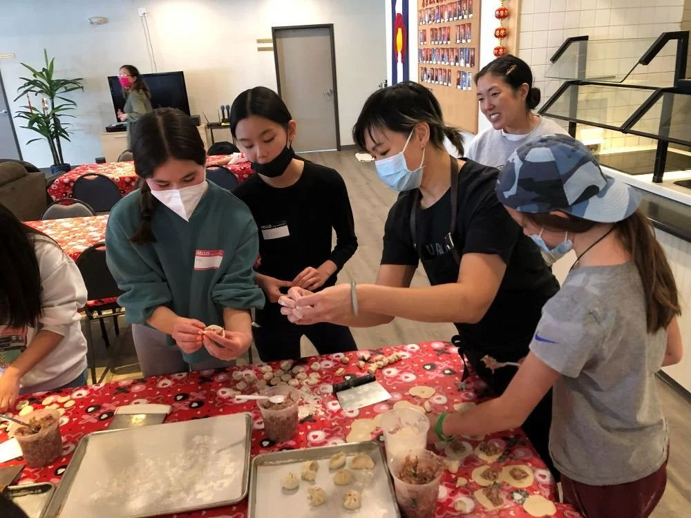 Chef Penelope Wong of Yuan Wonton demonstrating dumpling folding to students at a red decorated table at AGI Dumpling Making Workshop 2022