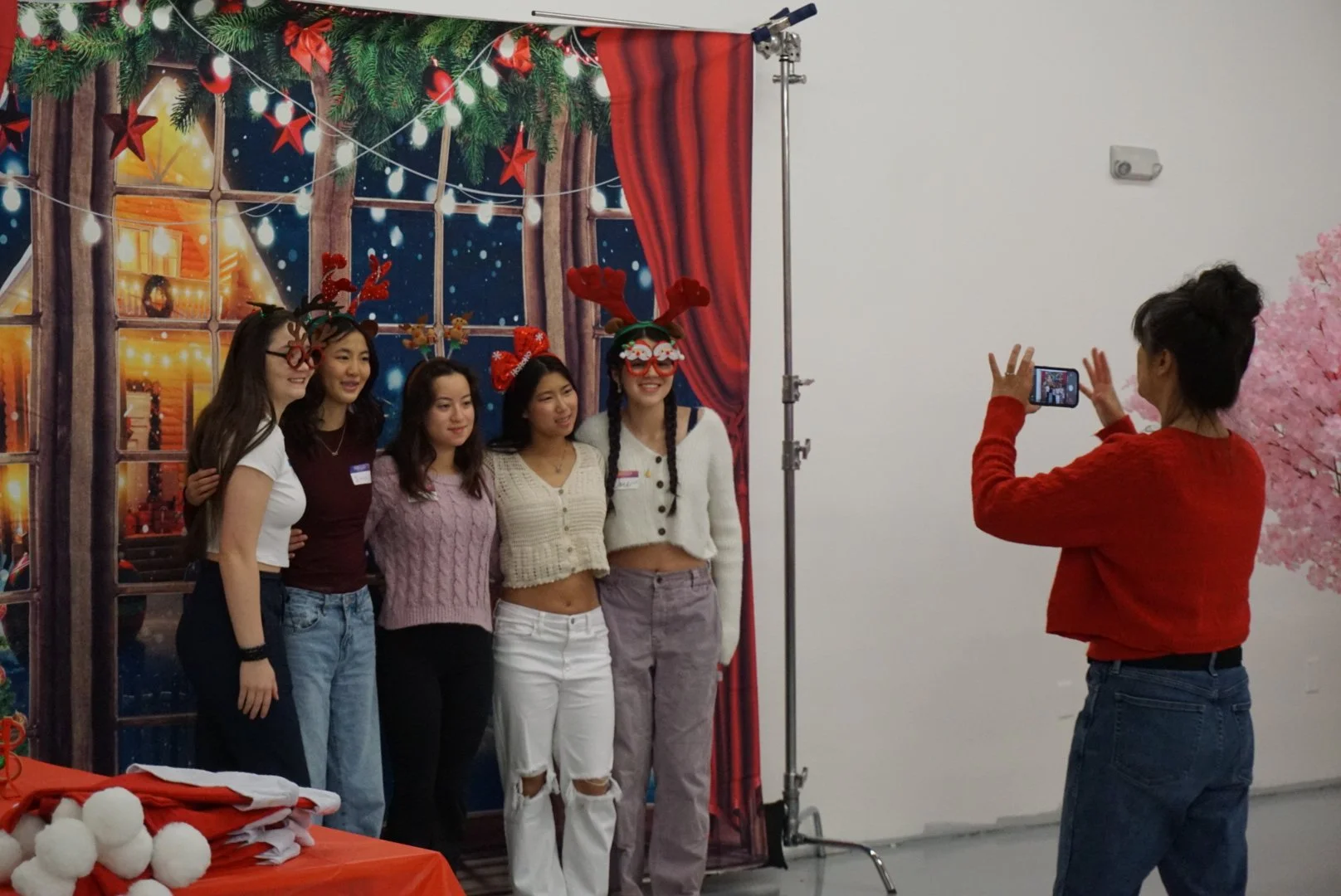  Students standing in front of holiday backdrop for photo with photobooth accessories getting photo taken at AGI Holiday Social 