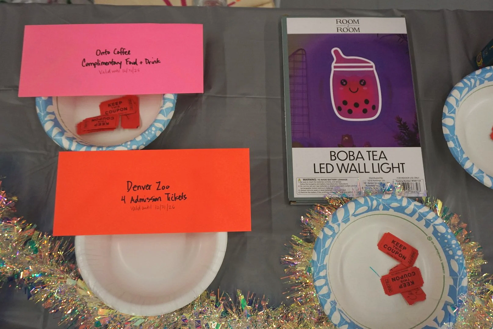  Bowls of raffle prizes with red tickets inside, packaged boba wall lamp above raffle bowl on gray table with tinsel decor 