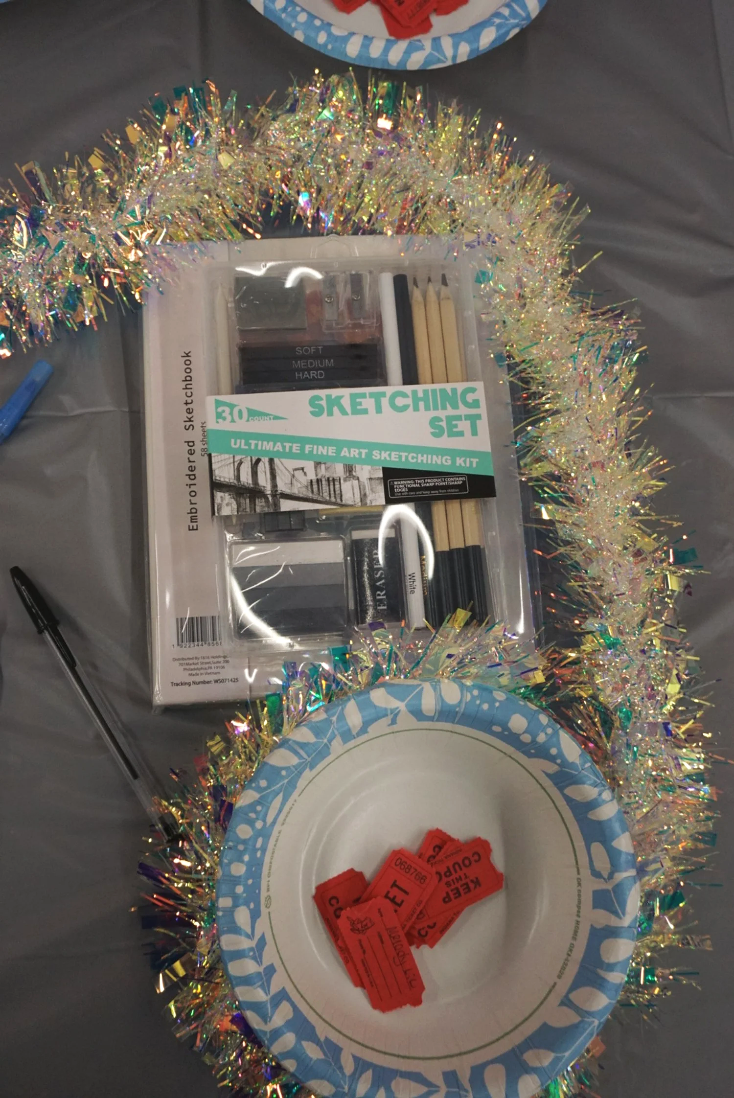  Sketchbook set above paper bowl with tickets for raffle on gray table with tinsel decor 